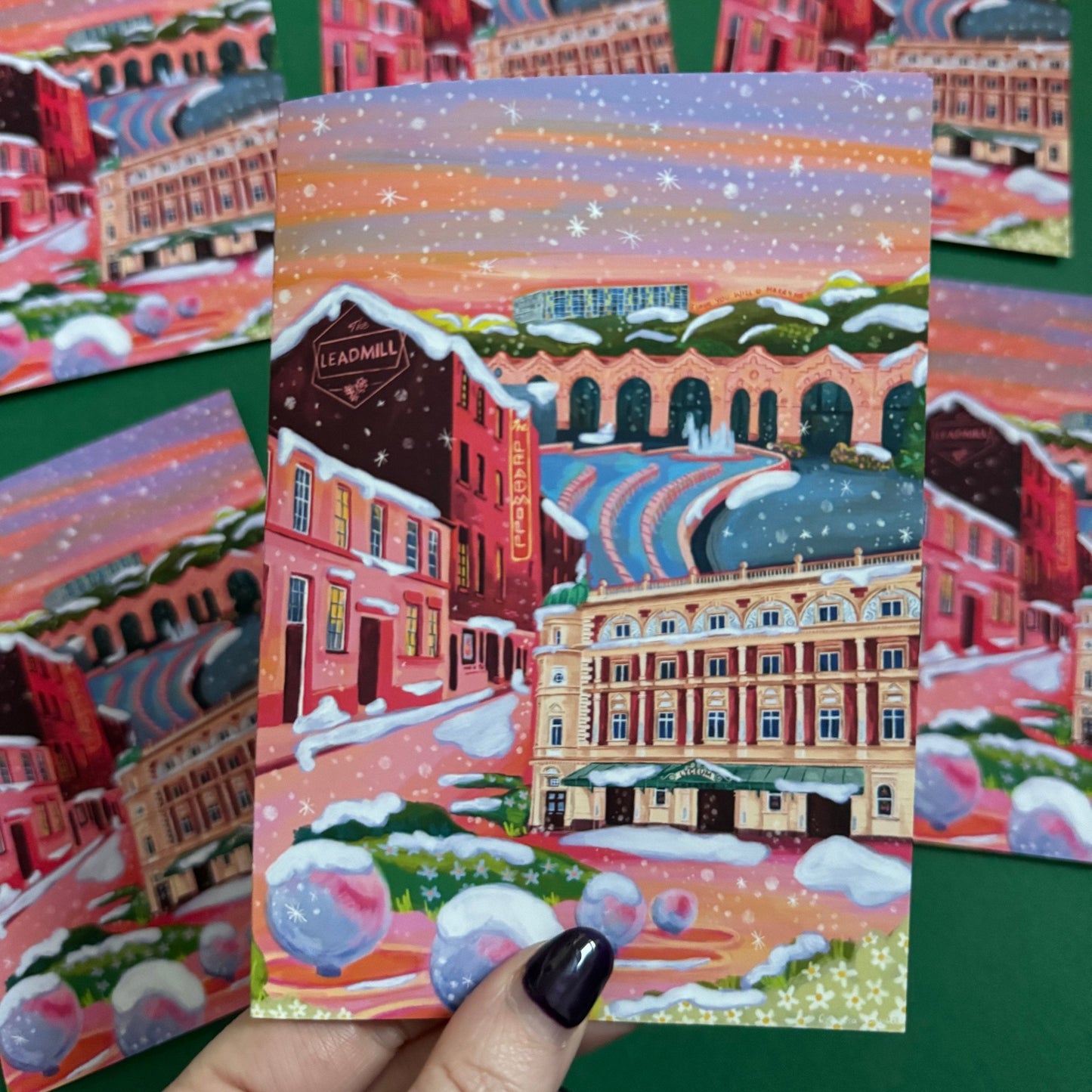 An illustrated greeting card of Sheffield city in winter with snow. Featuring The Leadmill, the Lyceum, Sheffield train station, Sheffield Park Hill flats, park hill graffiti and water features. This illustration is very vibrant with bright pinks and oranges, the places featured are collaged together against a purple and orange sky. There is a small signature in white the corner. Designed by Rebecca Gibbs at Rebecca Elizabeth Draws.