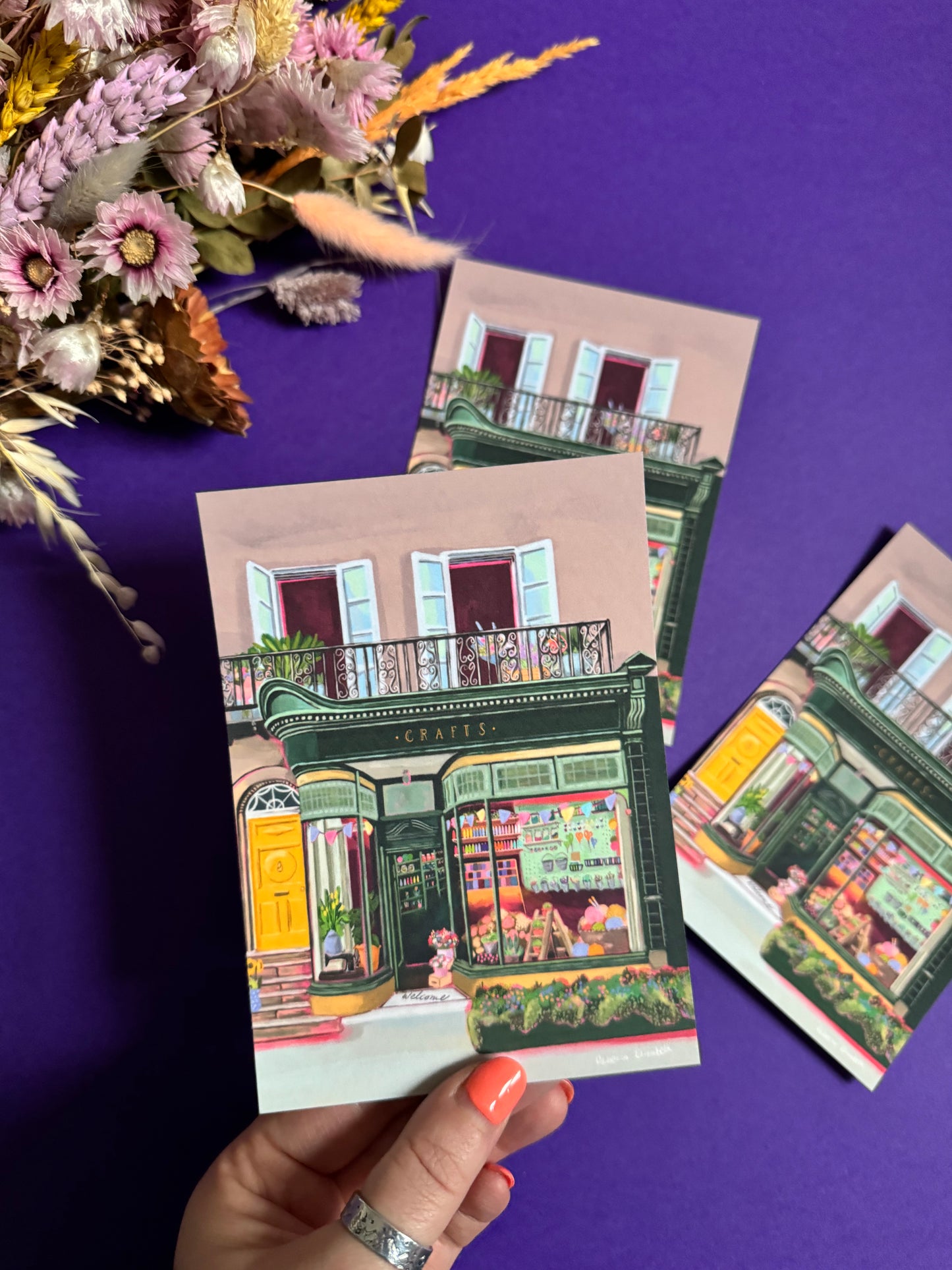 A colourful illustration of a craft shop with the store front in green and looking through the window and at all the goodies. Sewing, drawing, painting, we have it all here at the craft shop. Designed by Rebecca Elizabeth draws.