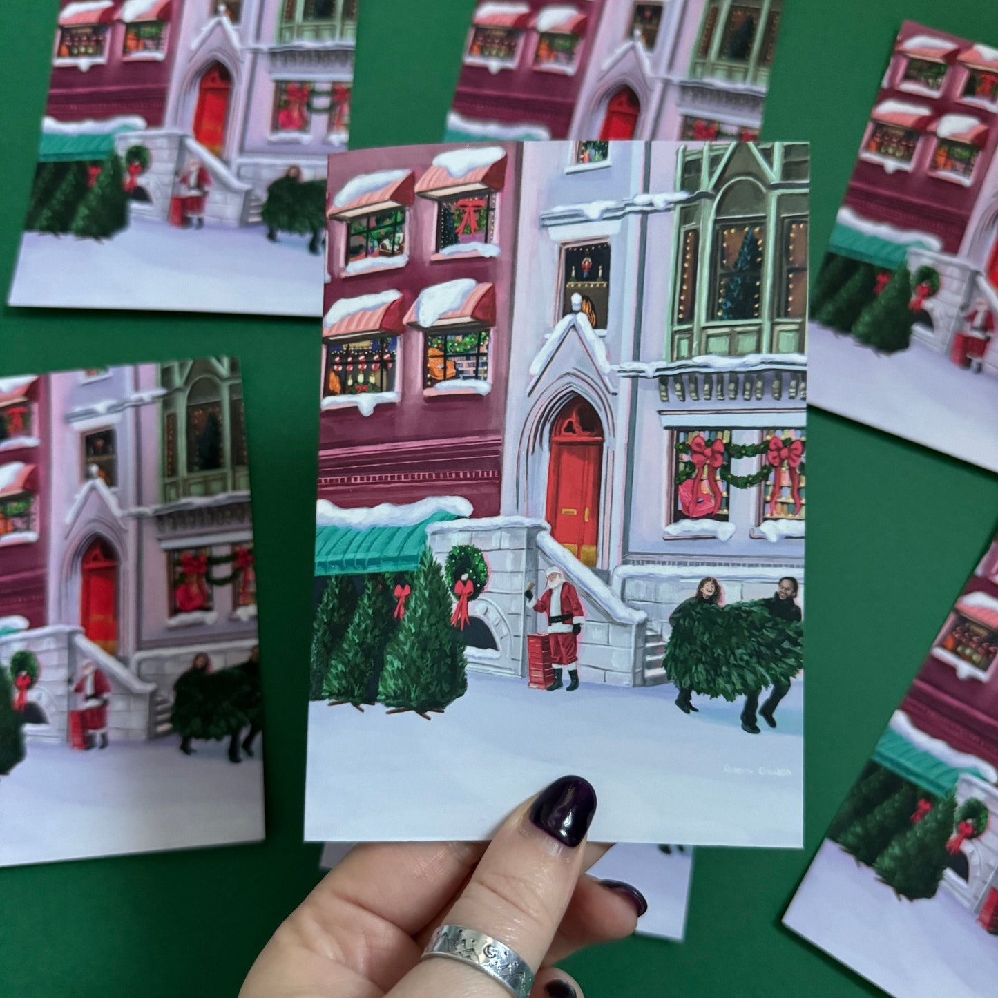 Christmas Illustration inspired by the film When Harry Met Sally. With Harry & Sally running off with their Christmas tree at the right hand side, the tree shop to the left and a background of new York buildings with Christmas décor peaking out the windows. Christmas card with red back designed by Rebecca Gibbs at Rebecca Elizabeth Draws.