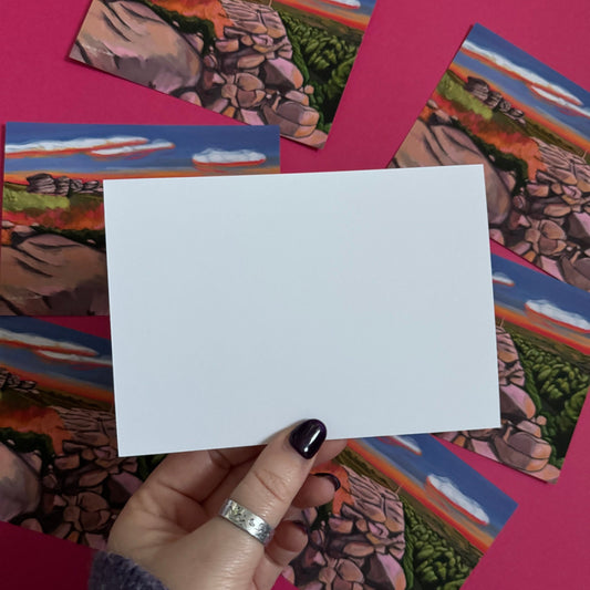 An illustrated postcard of Birchen Edge in the Peak District. With the rock face, rock outcrops named after ships from the battle of Trafalgar and Nelsons Monument all set against a sunset sky with blue, yellow, orange, and pink glow.