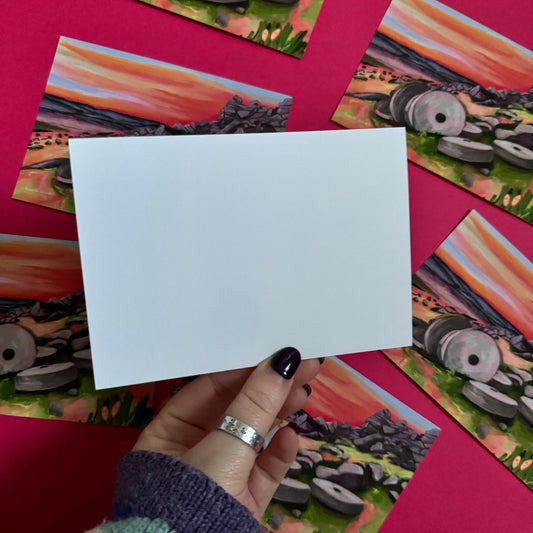 Colourful illustrated postcard of the millstones at Stanage edge in Derbyshire. With lots of pinks, greens and greys and a sunset sky. Designed by Rebecca Elizabeth Draws.