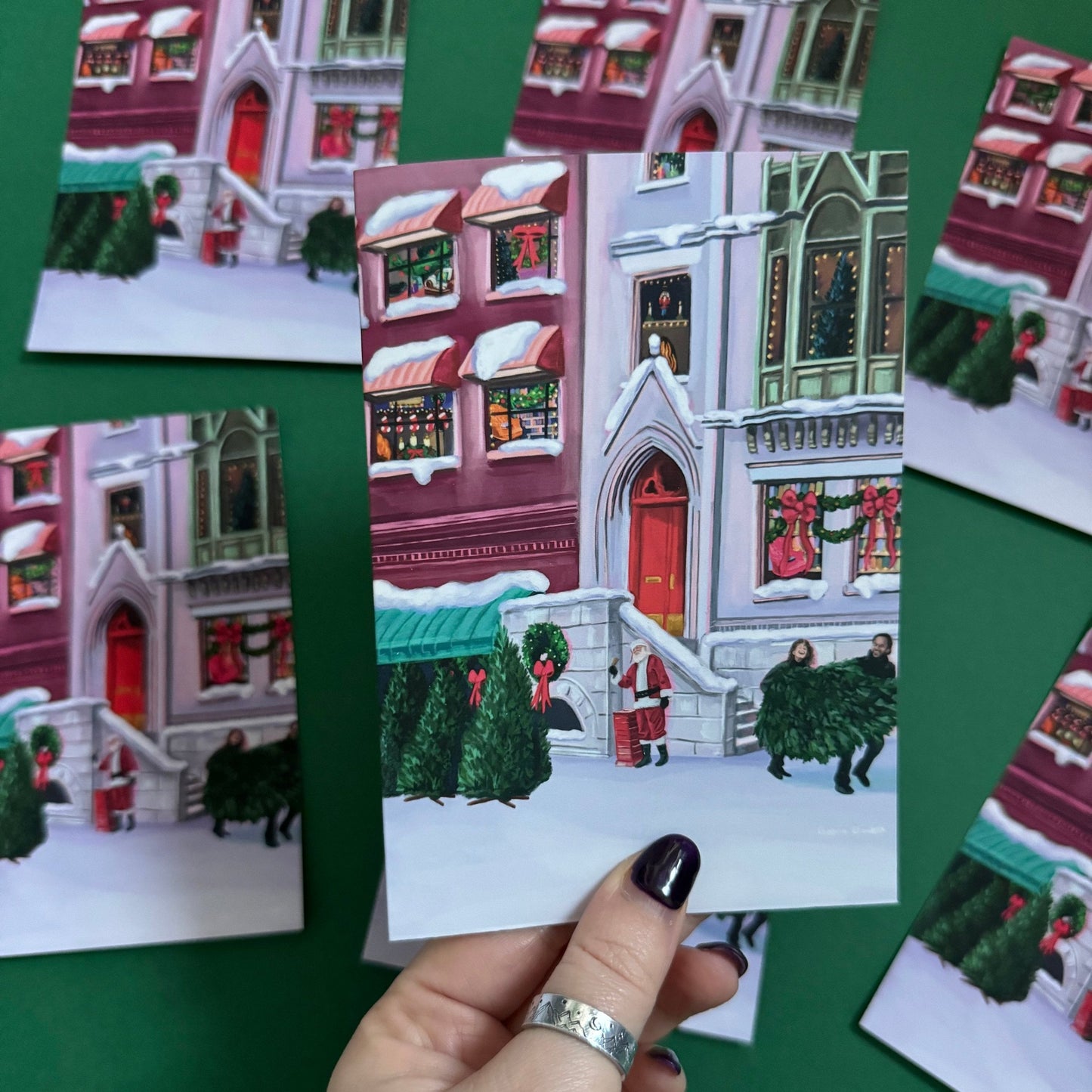 Christmas Illustration inspired by the film When Harry Met Sally. With Harry & Sally running off with their Christmas tree at the right hand side, the tree shop to the left and a background of new York buildings with Christmas décor peaking out the windows. Christmas card with red back designed by Rebecca Gibbs at Rebecca Elizabeth Draws.