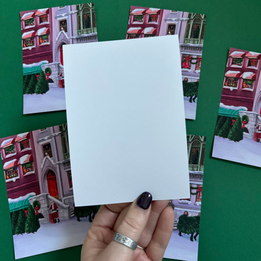 Christmas Illustrated postcard inspired by the film When Harry Met Sally. With Harry & Sally running off with their Christmas tree at the right hand side, the tree shop to the left and a background of new York buildings with Christmas décor peaking out the windows. Designed by Rebecca Gibbs at Rebecca Elizabeth Draws.