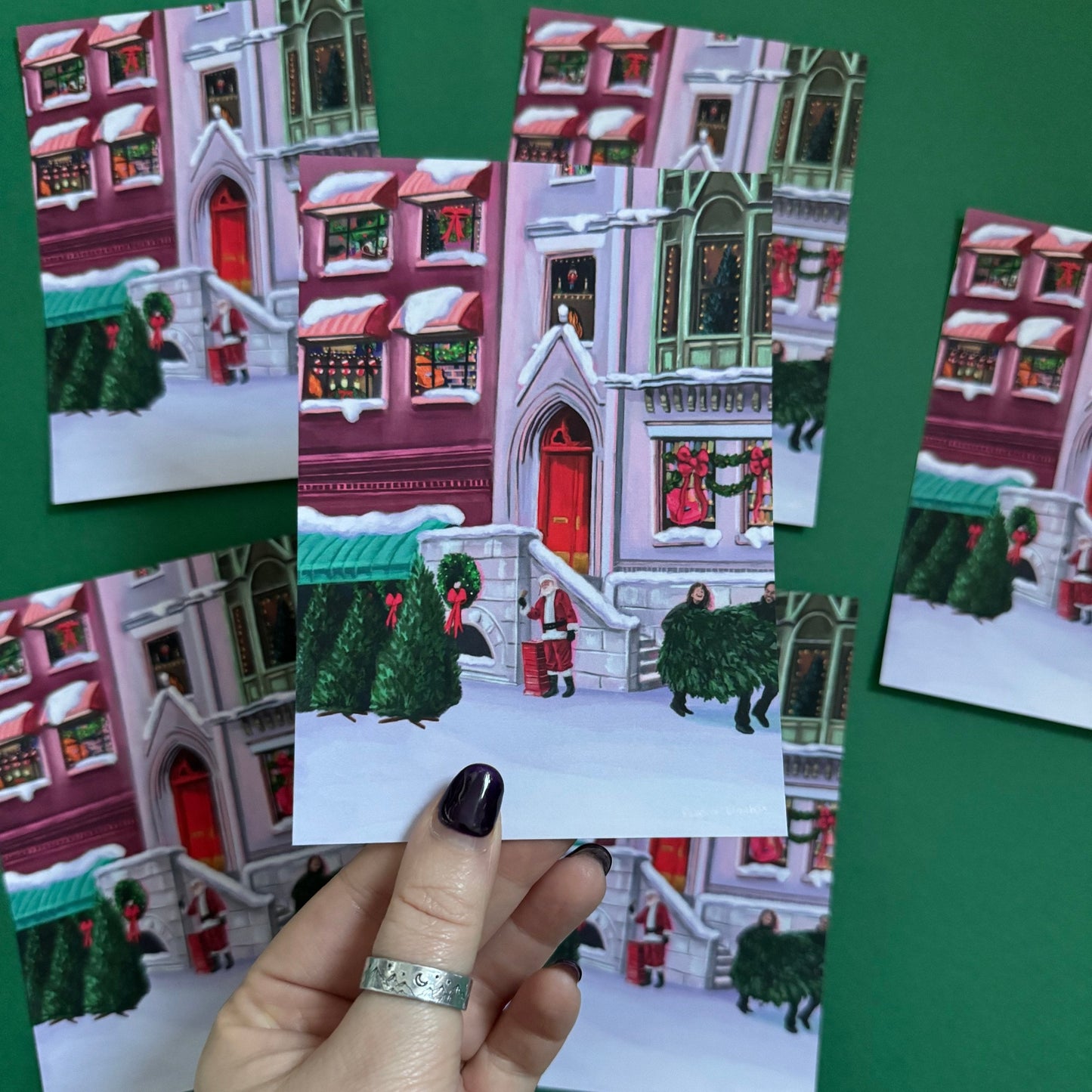 Christmas Illustrated postcard inspired by the film When Harry Met Sally. With Harry & Sally running off with their Christmas tree at the right hand side, the tree shop to the left and a background of new York buildings with Christmas décor peaking out the windows. Designed by Rebecca Gibbs at Rebecca Elizabeth Draws.