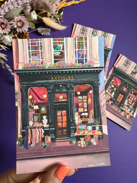Illustration of a antiques shop front in black with ornate designs, inside is pink and golden with vintage objects such a clocks, statues, picture frames. The illustration gives off dark academia vibes. Designed by Rebecca Elizabeth Draws.