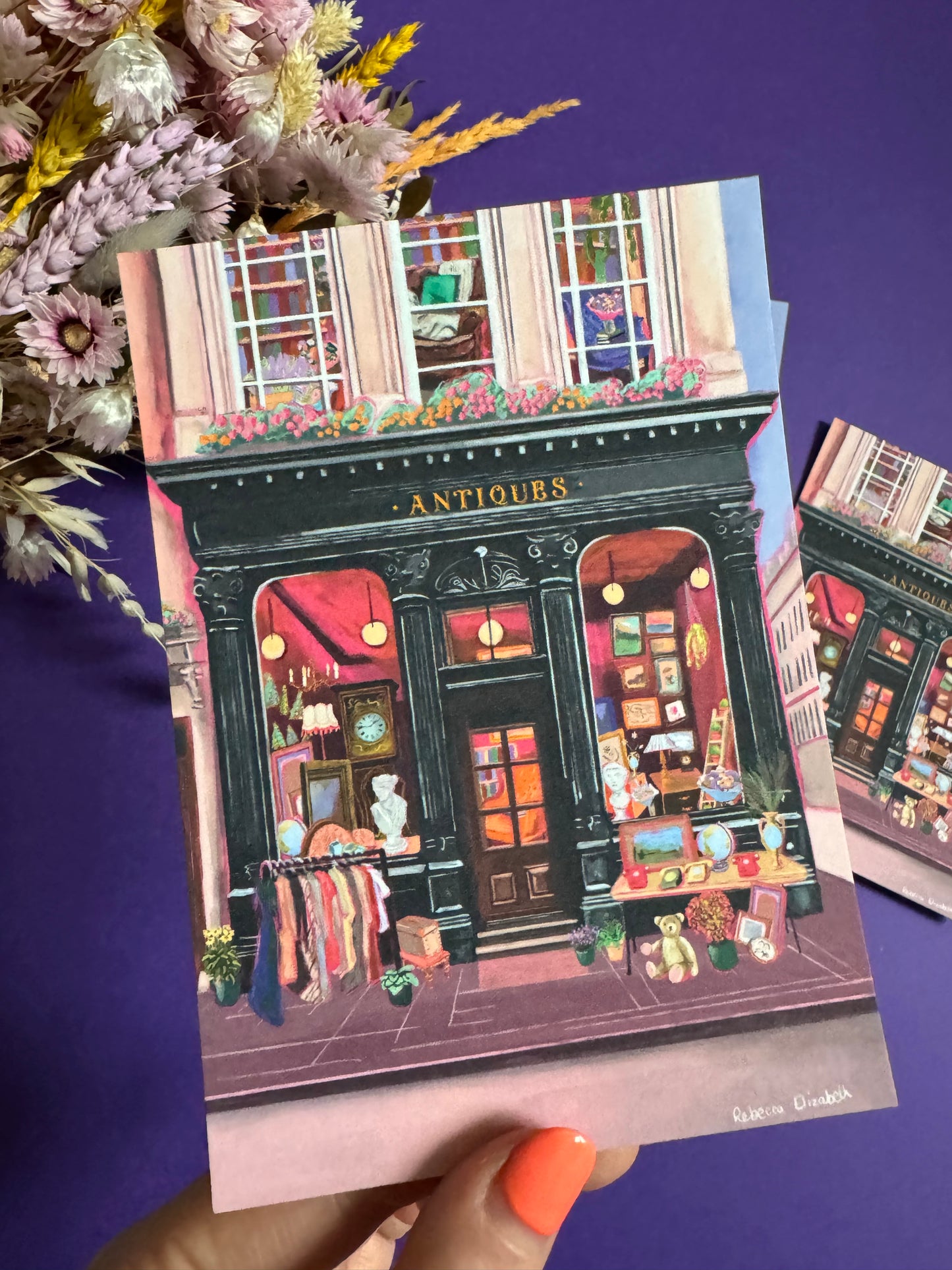 Illustration of a antiques shop front in black with ornate designs, inside is pink and golden with vintage objects such a clocks, statues, picture frames. The illustration gives off dark academia vibes. Designed by Rebecca Elizabeth Draws.
