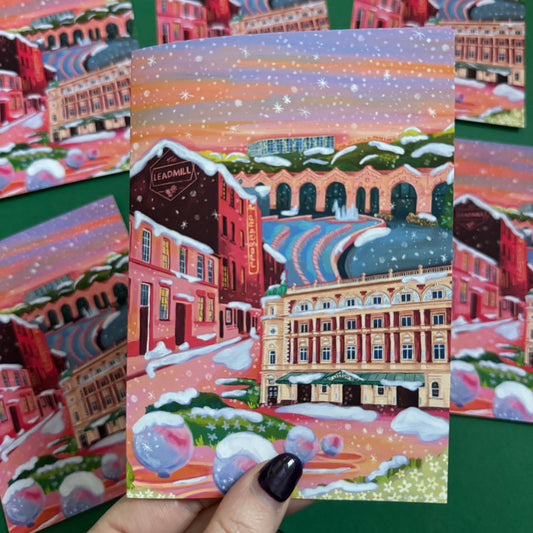 An illustrated greeting card of Sheffield city in winter with snow. Featuring The Leadmill, the Lyceum, Sheffield train station, Sheffield Park Hill flats, park hill graffiti and water features. This illustration is very vibrant with bright pinks and oranges, the places featured are collaged together against a purple and orange sky. There is a small signature in white the corner. Designed by Rebecca Gibbs at Rebecca Elizabeth Draws.