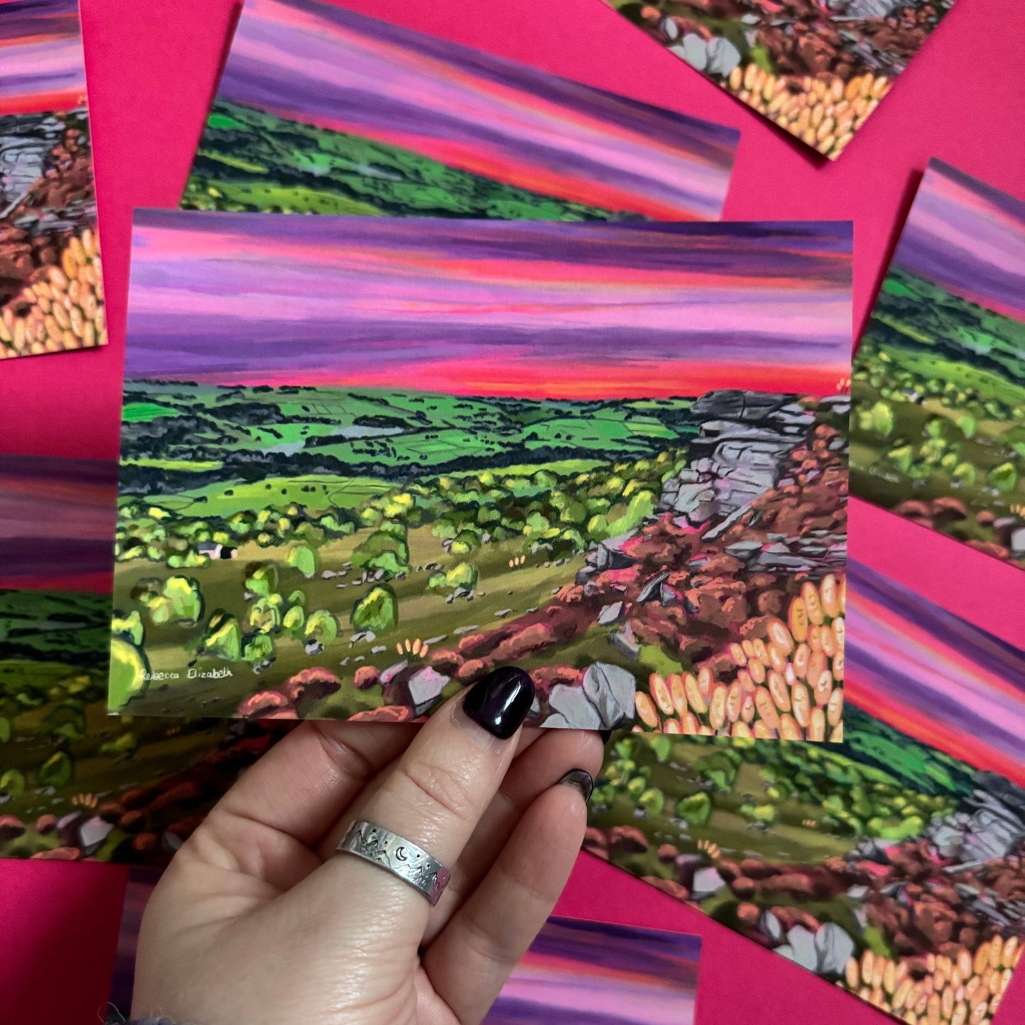 A colourful illustration of Curbar edge, Derbyshire with the rock formation to the right covered in pink and golden flowers, yellow flowers in the foreground and then rolling hills to the left with lots of greenery and trees. A stunning bright pink and purple sunset across the sky. Designed by
Rebecca Elizabeth draws. Rebecca Elizabeth draws.