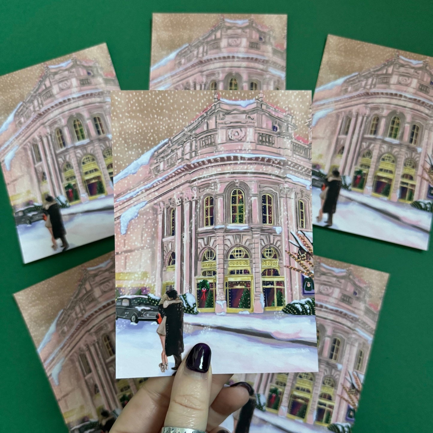 Christmas Illustrated postcard inspired by the film Bridget Jones Diary. The end scene featuring Mark Darcy & Bridget Jones kissing in the snow on a hazy street in London in front of the Montblanc diary shop. In the background you can see the mini her friends drive away in and a poster with Marks reindeer Christmas jumper. A velvet laminated postcard. Designed by Rebecca Gibbs at Rebecca Elizabeth Draws.