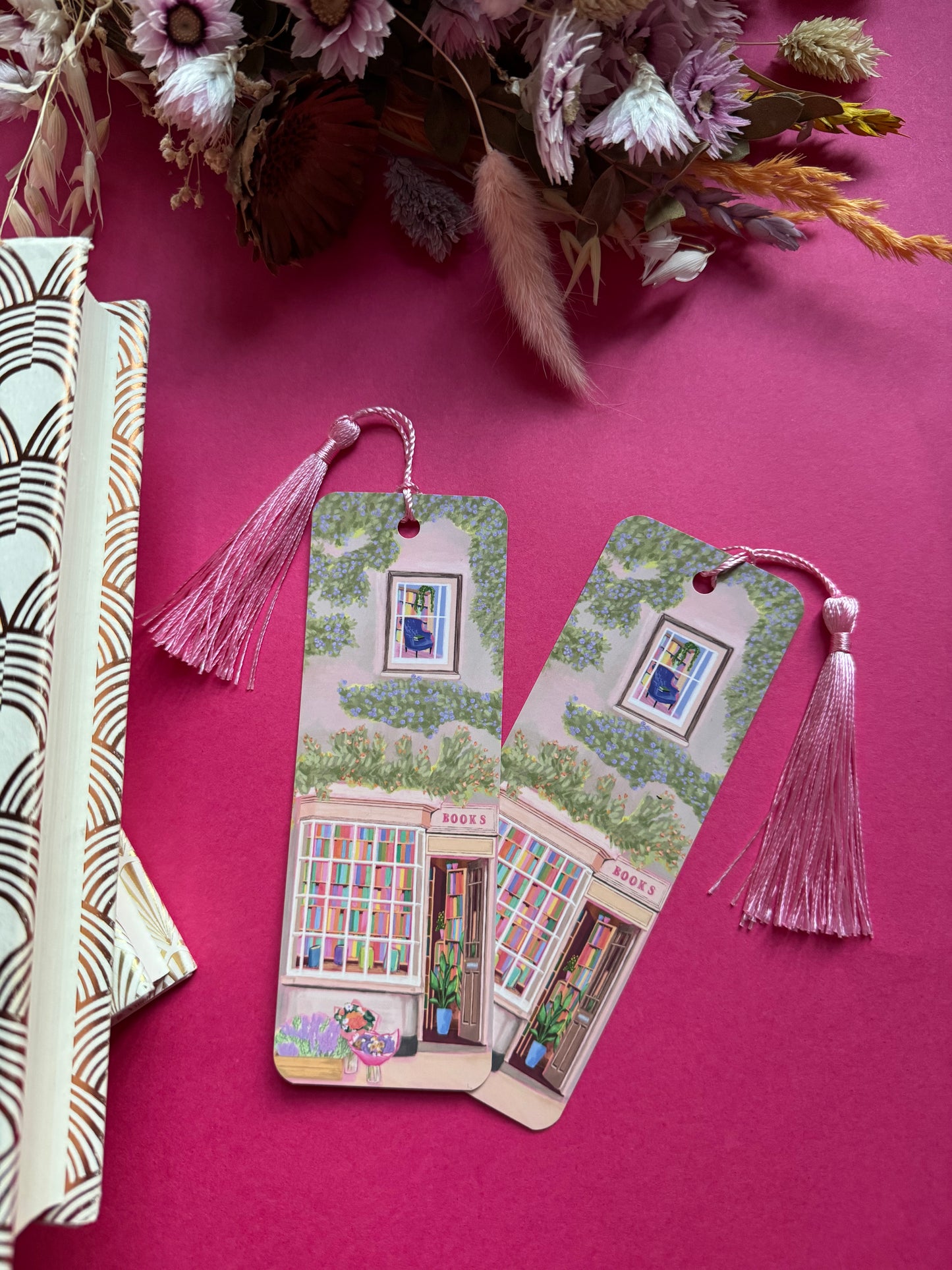 An illustrated bookmark of a cute cosy bookshop, the window shows the bookshelves inside full of bright coloured book spines. There are books placed stood up at the front. Outside the building is a soft colour with lots of greenery in soft pale greens and orange and lilac flowers. In front of the building there are plant pots and flowers. A whimsical cosy art bookmark. There is a small signature in white the corner. Designed by Rebecca Gibbs at Rebecca Elizabeth Draws.