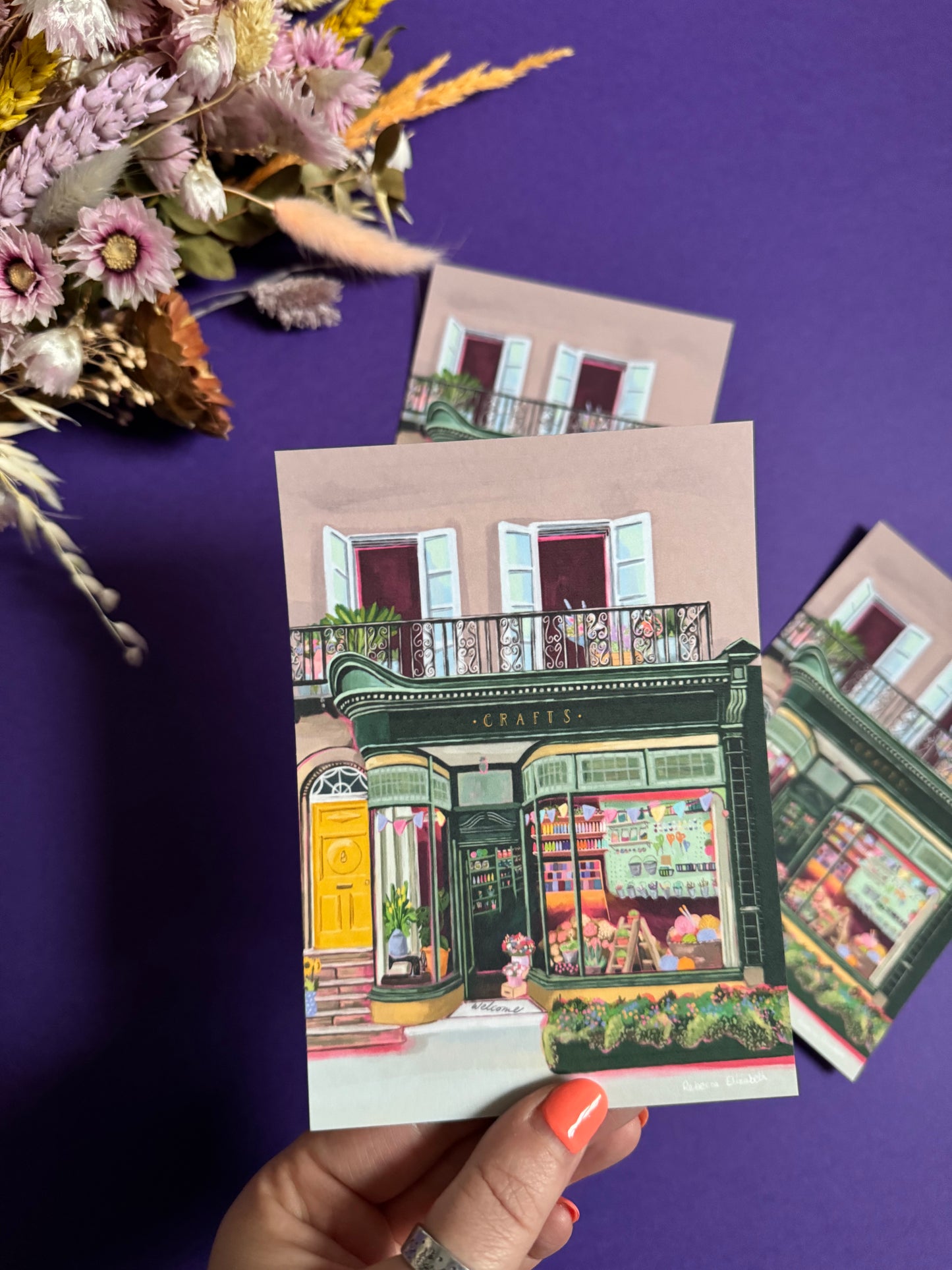A colourful illustration of a craft shop with the store front in green and looking through the window and at all the goodies. Sewing, drawing, painting, we have it all here at the craft shop. Designed by Rebecca Elizabeth draws.