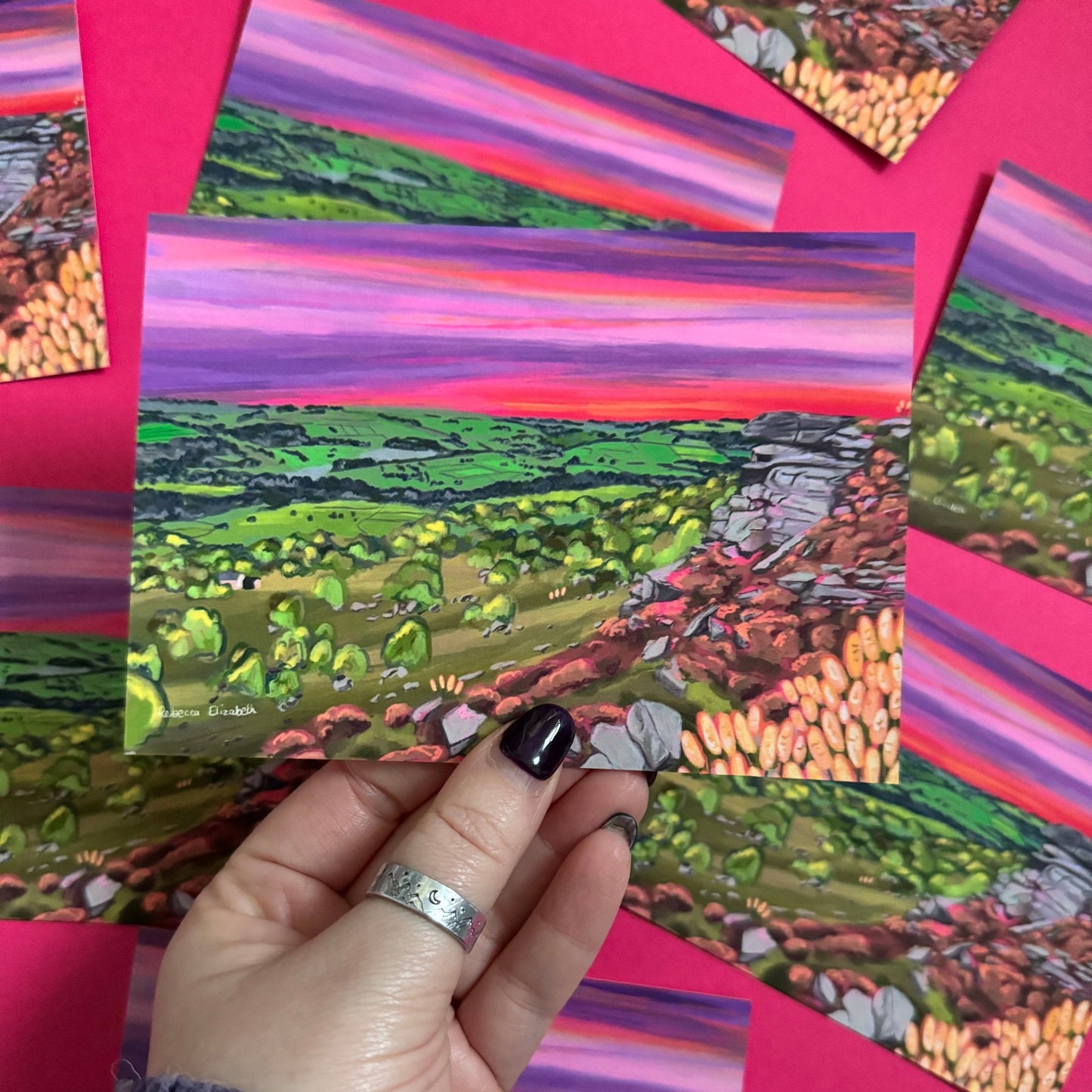 A colourful illustration of Curbar edge, Derbyshire with the rock formation to the right covered in pink and golden flowers, yellow flowers in the foreground and then rolling hills to the left with lots of greenery and trees. A stunning bright pink and purple sunset across the sky. Designed by
Rebecca Elizabeth draws.