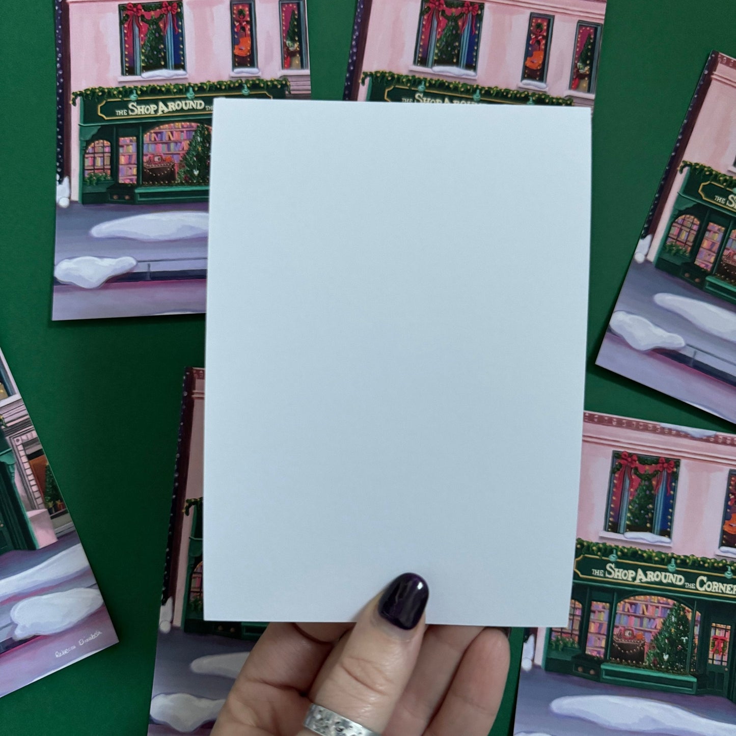 Christmas Illustrated postcard inspired by the film You’ve Got Mail. The Shop Around the Corner is a cosy & whimsical bookshop owned by Kathleen Kelly, inside is lots of fairy lights, Christmas trees, books and baubles. Outside you can see snow and inside the cosy windows with festive decor. Designed by Rebecca Gibbs at Rebecca Elizabeth Draws.