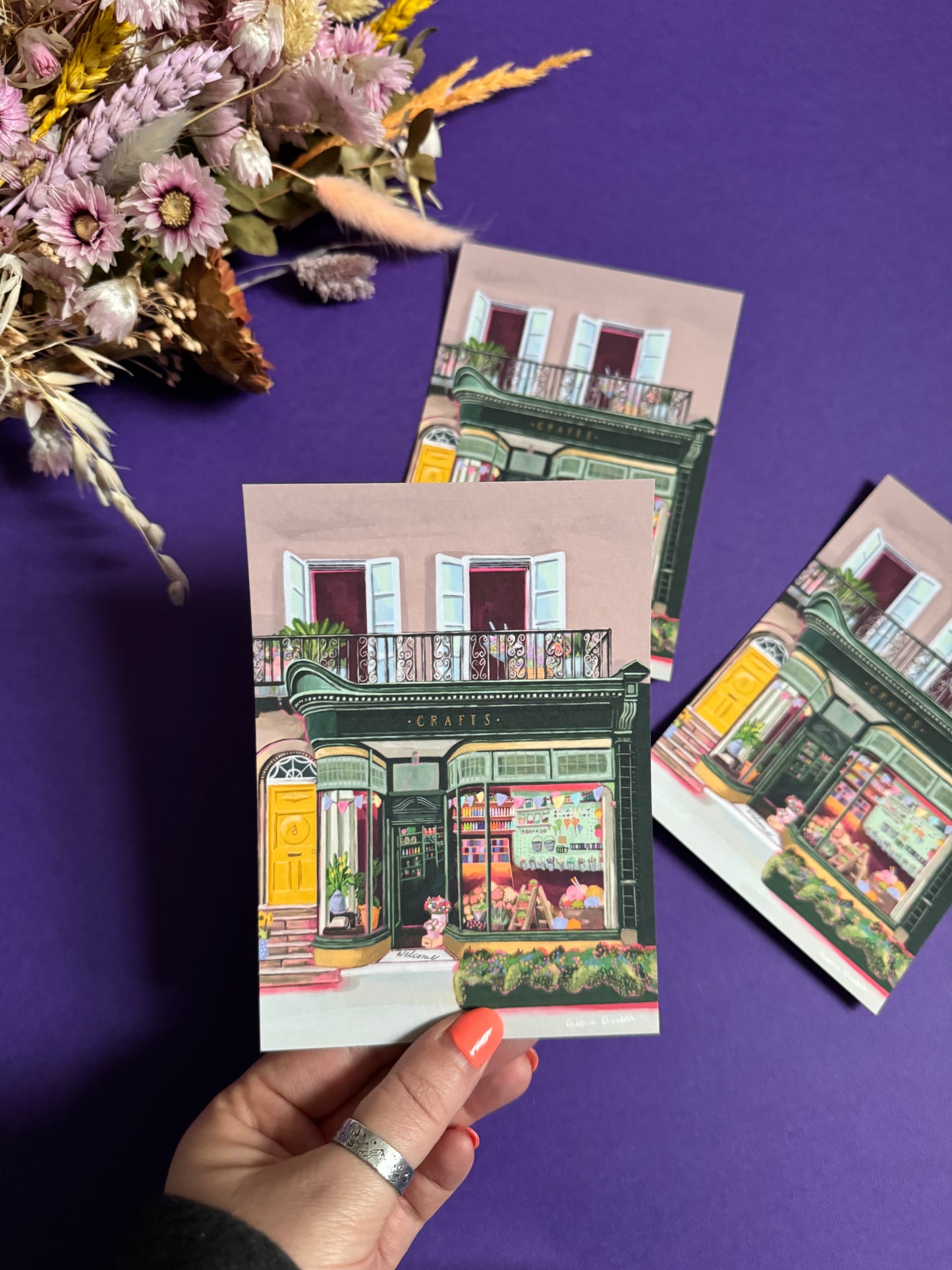 A colourful illustration of a craft shop with the store front in green and looking through the window and at all the goodies. Sewing, drawing, painting, we have it all here at the craft shop. Designed by Rebecca Elizabeth draws.