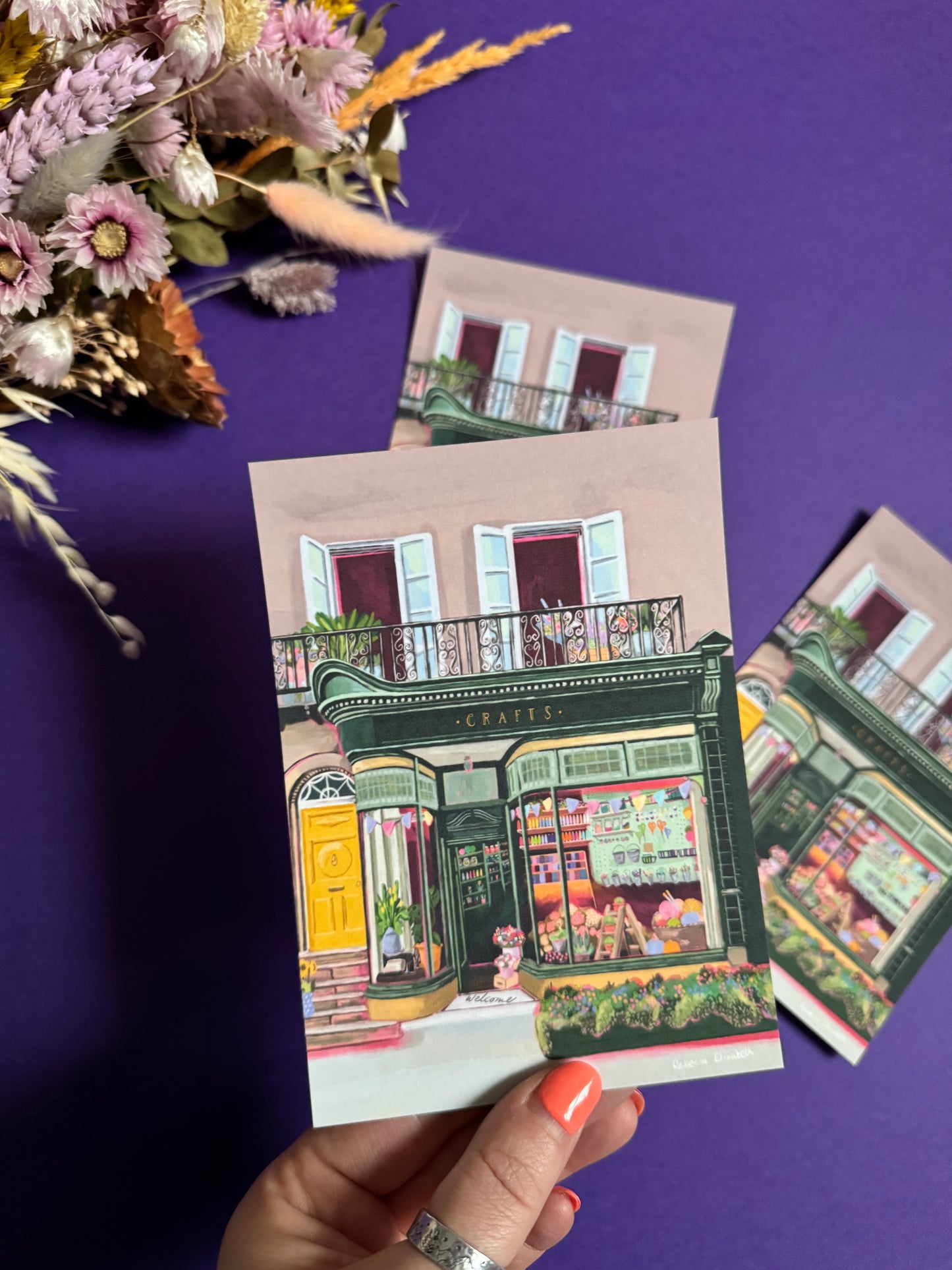 A colourful illustration of a craft shop with the store front in green and looking through the window and at all the goodies. Sewing, drawing, painting, we have it all here at the craft shop. Designed by Rebecca Elizabeth draws.