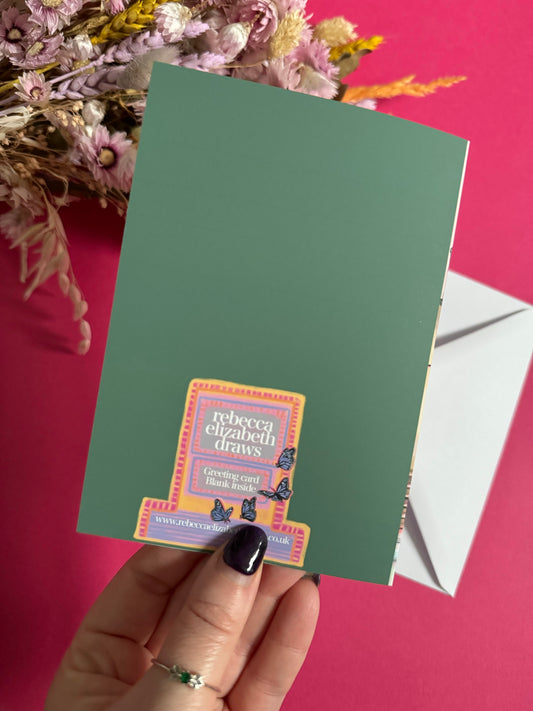 Pink shop front of a plant store on a greeting card with lots of greenery inside, a balcony above with windows showing chairs and a bookcase and more flowers. A yellow door to the side with a sunflower vase resting on the steps by Rebecca Elizabeth Draws.