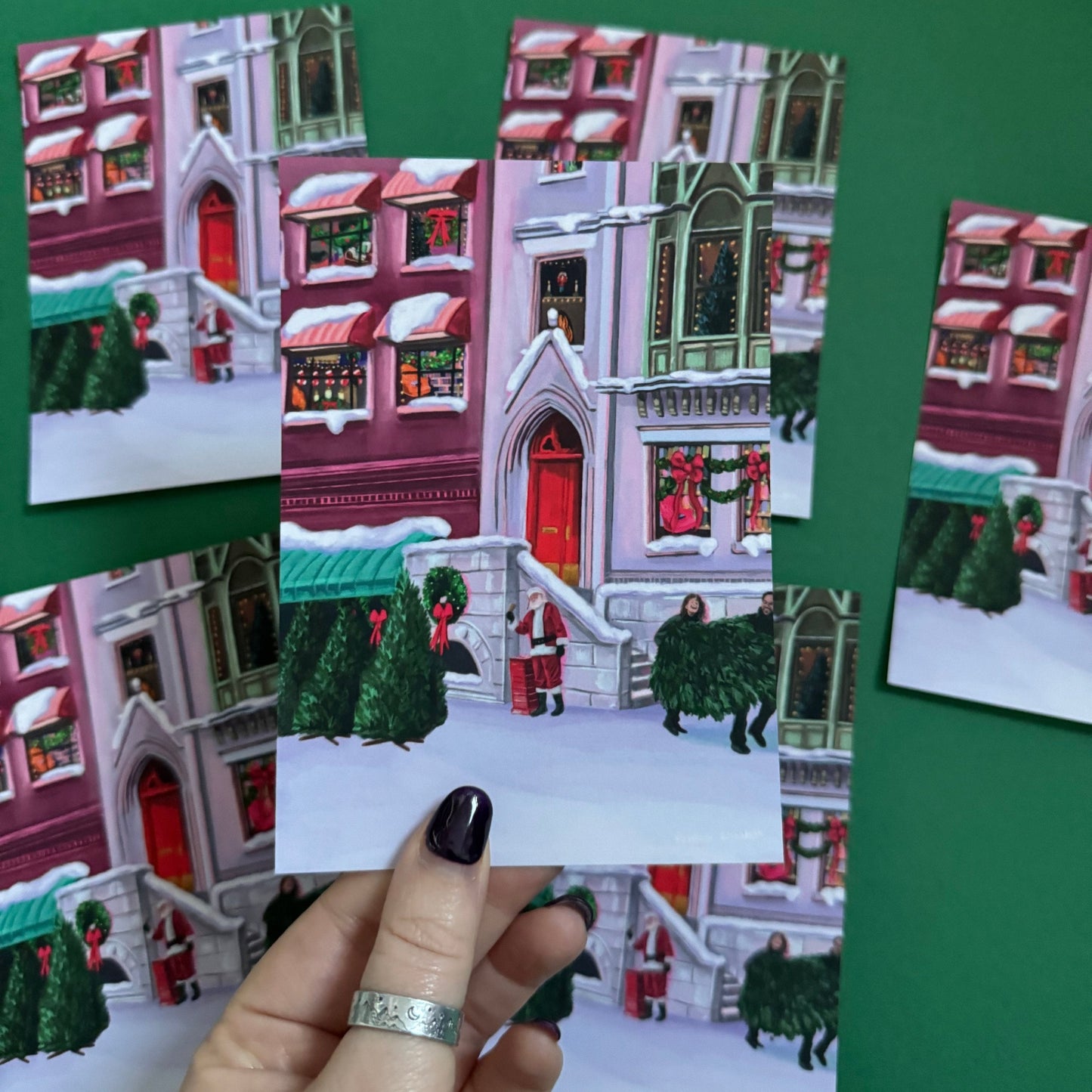 Christmas Illustrated postcard inspired by the film When Harry Met Sally. With Harry & Sally running off with their Christmas tree at the right hand side, the tree shop to the left and a background of new York buildings with Christmas décor peaking out the windows. Designed by Rebecca Gibbs at Rebecca Elizabeth Draws.