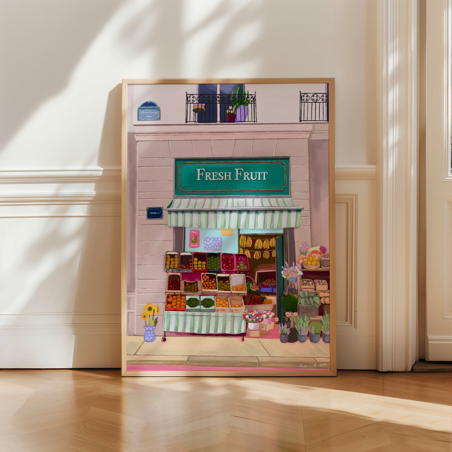Illustration of a fabulous fruit shop, baskets of fruit line outside the shop, a canopy in mint green & white hangs over & inside you can see boxes of fruit & bananas hanging. The wall has a sign strawberry lane & there is a balcony upstairs.