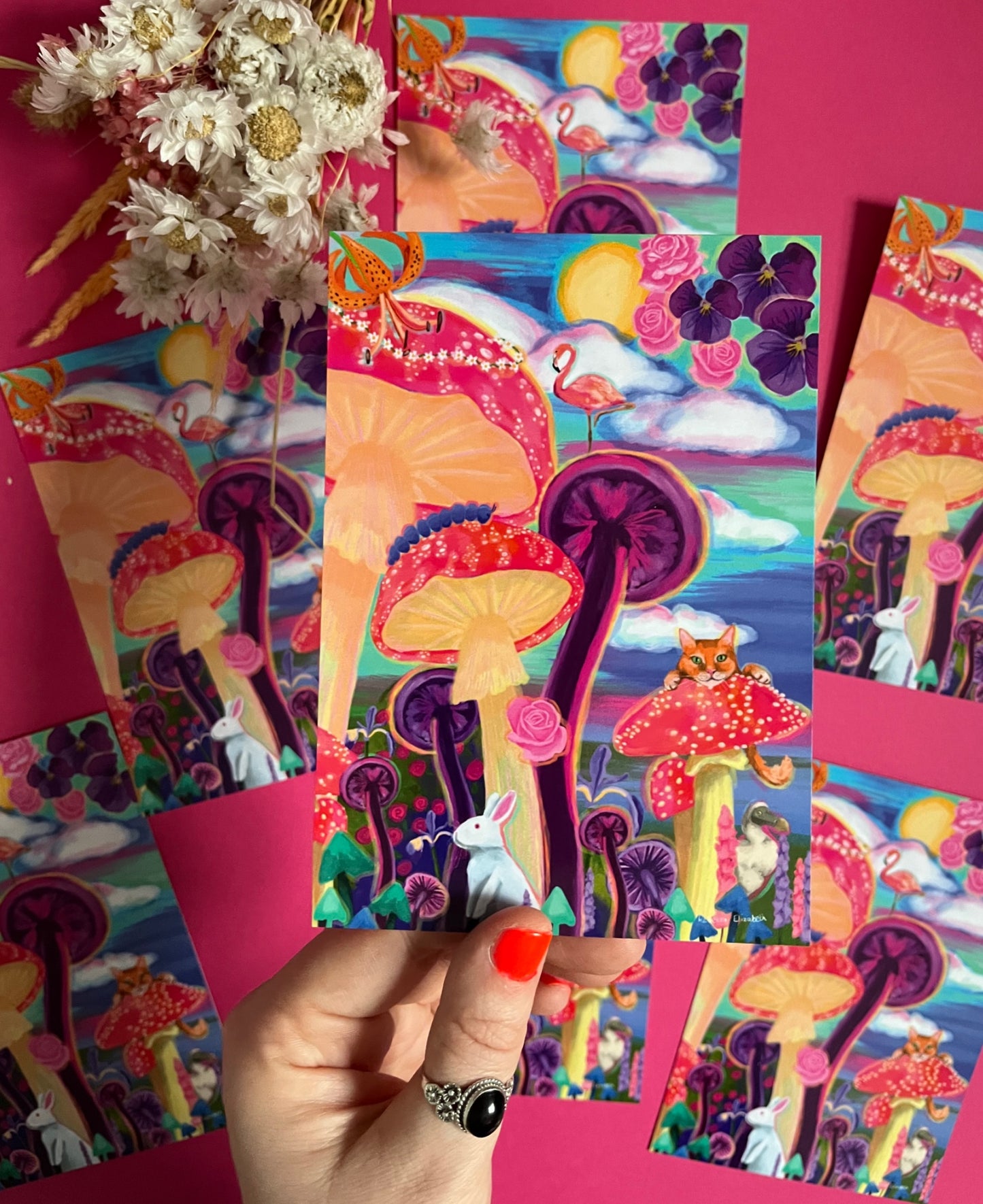 Postcard of colourful Alice in Wonderland inspired illustration. Trippy toadstools, flowers, and classic animals featured from the children’s book such as the Cheshire cat and the dodo. Vibrant blues, pinks and purples. Designed by Rebecca Elizabeth Draws.