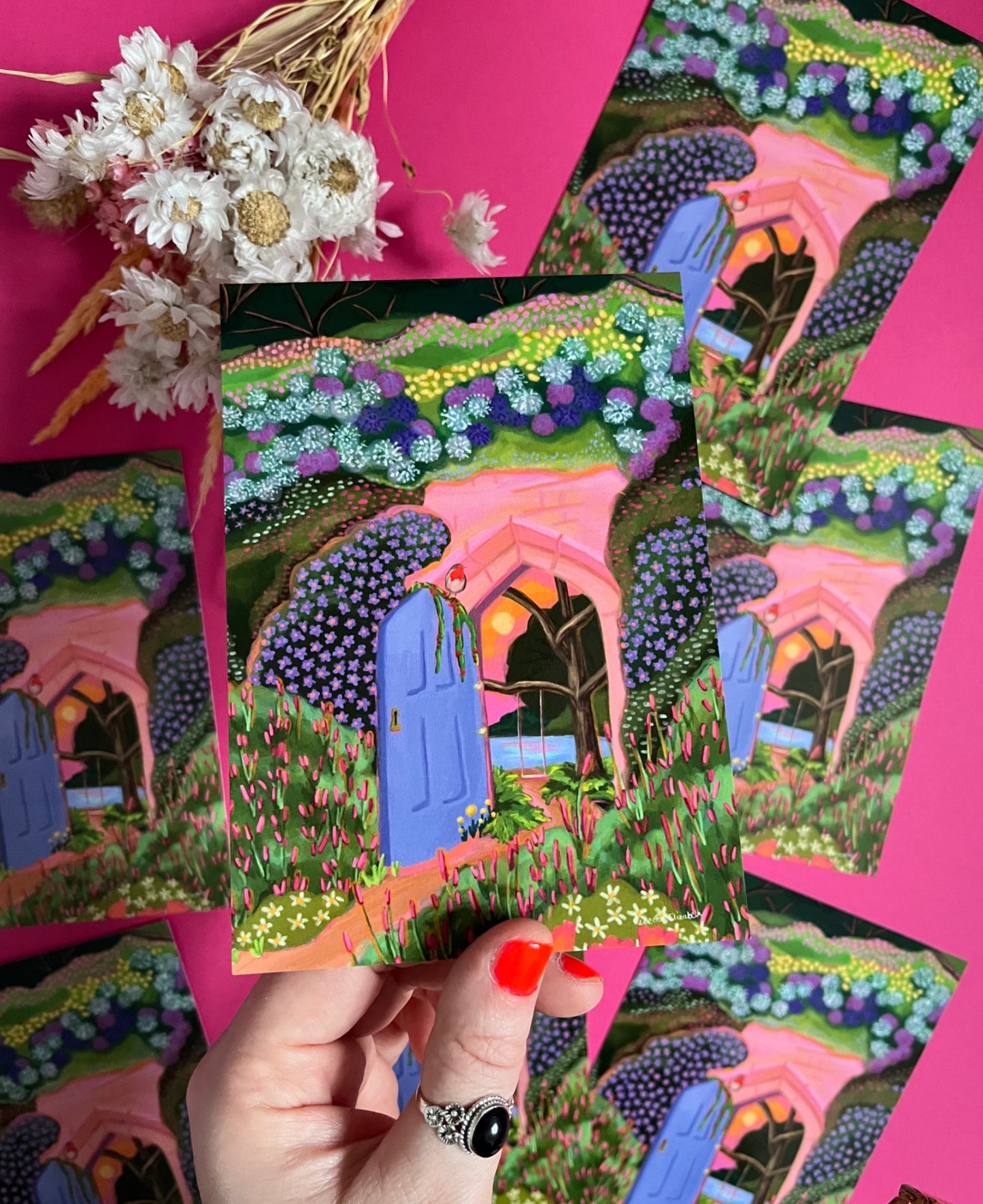 Postcard art inspired by the children’s book The Secret Garden with a door leading to a hidden paradise. A swing over the pond, a setting sun and the foreground outside is engulfed in wildflowers. There is a robin perched on the door. Designed by Rebecca Elizabeth Draws.