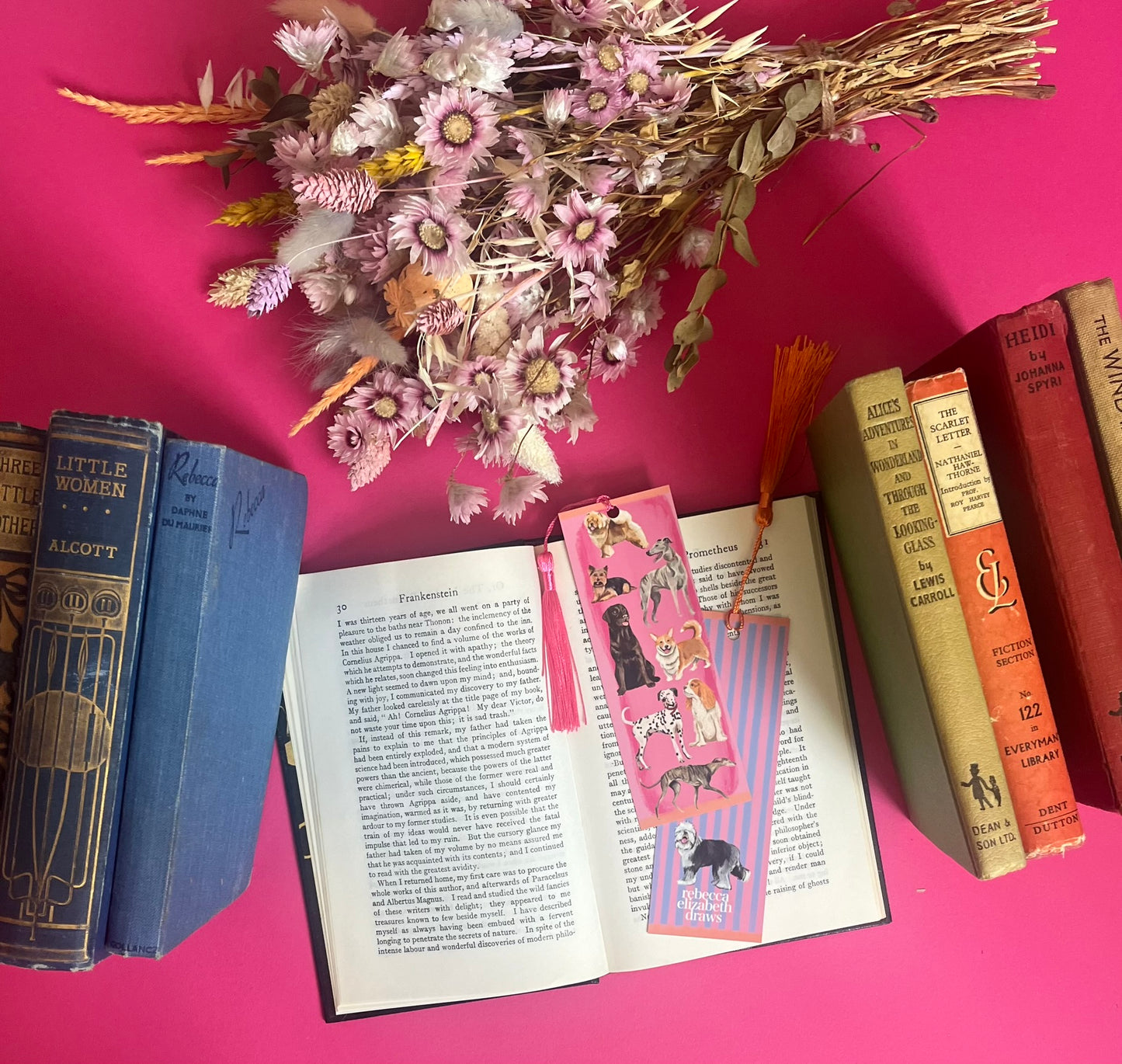 Hand drawn illustration of dogs, from whippets, lurchers, Labradors, Yorkshire terriers & more. All drawn in a collection on a pink background with pink and purple stripes on a bookmark with a pink & purple background & the Rebecca Elizabeth Draws logo.