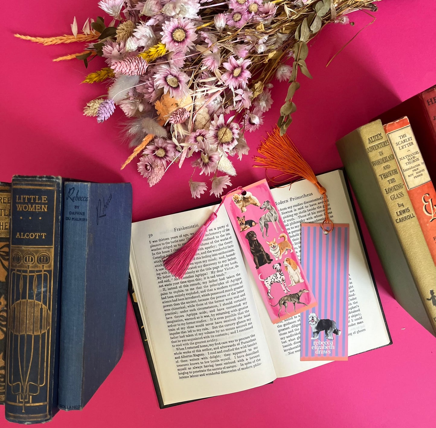 Hand drawn illustration of dogs, from whippets, lurchers, Labradors, Yorkshire terriers & more. All drawn in a collection on a pink background with pink and purple stripes on a bookmark with a pink & purple background & the Rebecca Elizabeth Draws logo.