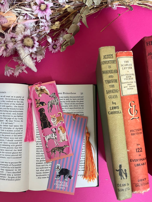 Hand drawn illustration of dogs, from whippets, lurchers, Labradors, Yorkshire terriers & more. All drawn in a collection on a pink background with pink and purple stripes on a bookmark with a pink & purple background & the Rebecca Elizabeth Draws logo.
