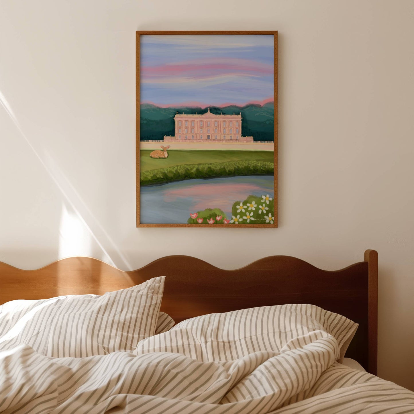 An illustration of Chatsworth house, a stately home found in the Derbyshire Dales. The house is a soft pink surrounded by green trees and fields, a river runs along the front and a deer rests in the foreground. The sky is a soft blue and pink hue, the colours of a beautiful sunset. A small signature in white the corner. Designed by Rebecca Gibbs at Rebecca Elizabeth Draws.