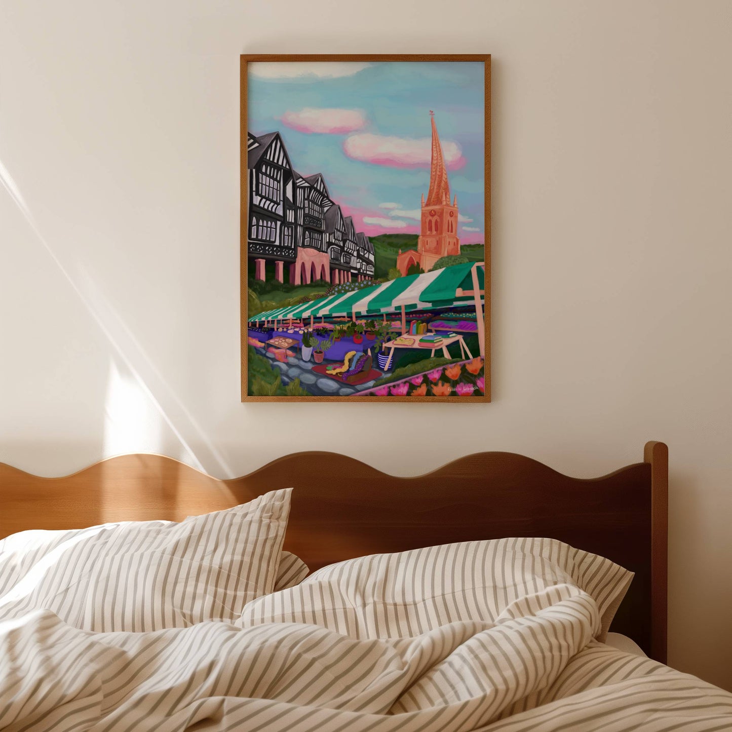 An illustration of the Derbyshire town Chesterfield. A summer illustration featuring the famous crooked spire, market stalls and Tudor buildings. Soft blue sky with fluffy clouds, this art piece is a soft representation of the market town. A small signature in white the corner. Designed by Rebecca Gibbs at Rebecca Elizabeth Draws.