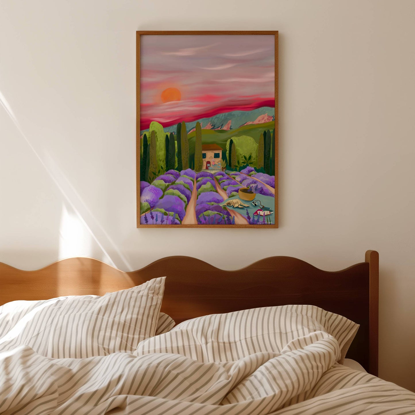 Lavender fields Provence, France. Purple lavender flowers leading to the centre. A picnic blanket with a dog, camera & books alongside a basket full of picked flowers. The centre features a house, big green trees & mountains set against a pink sky.