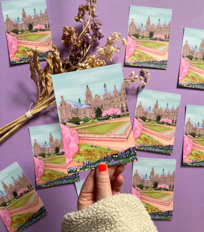 An illustration of the view of the Peace Gardens, Sheffield city centre in springtime. A soft brown building of Sheffield’s town hall with trees in front and pink blossom trees in soft pinks. The foreground features the peace garden with patches of grass and then flowers in yellows and purples underneath another pink blossom tree in the front and a baby blue sky. There is a small signature in white the corner.  Designed by Rebecca Gibbs on a postcard at Rebecca Elizabeth Draws.