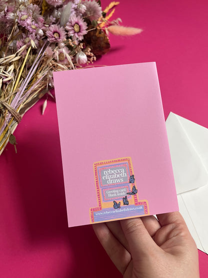 An illustration of a cute whimsical bookshop, the window shows the bookshelves inside full of bright coloured book spines with lots of flowers. The back of the card is pink with the Rebecca Elizabeth Draws logo. 