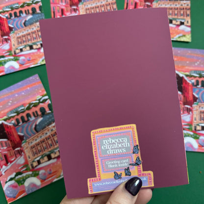 An illustrated greeting card of Sheffield city in winter with snow. Featuring The Leadmill, the Lyceum, Sheffield train station, Sheffield Park Hill flats, park hill graffiti and water features. This illustration is very vibrant with bright pinks and oranges, the places featured are collaged together against a purple and orange sky. There is a small signature in white the corner.  Designed by Rebecca Gibbs at Rebecca Elizabeth Draws.