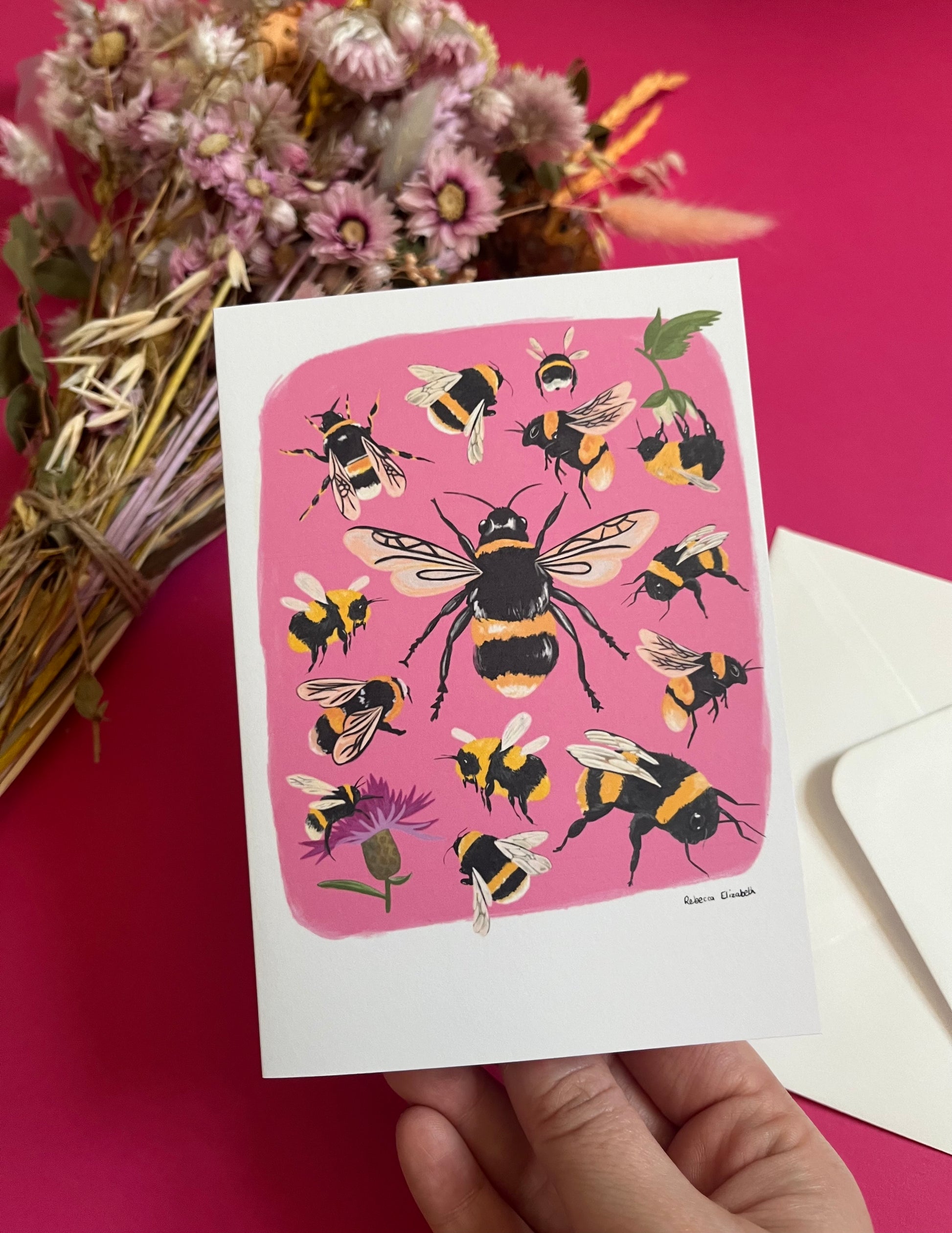 Hand painted bumble bee illustrations compiled together on a pink background, small bees big bees, bees with flowers. The back of the card is green with the Rebecca Elizabeth Draws logo