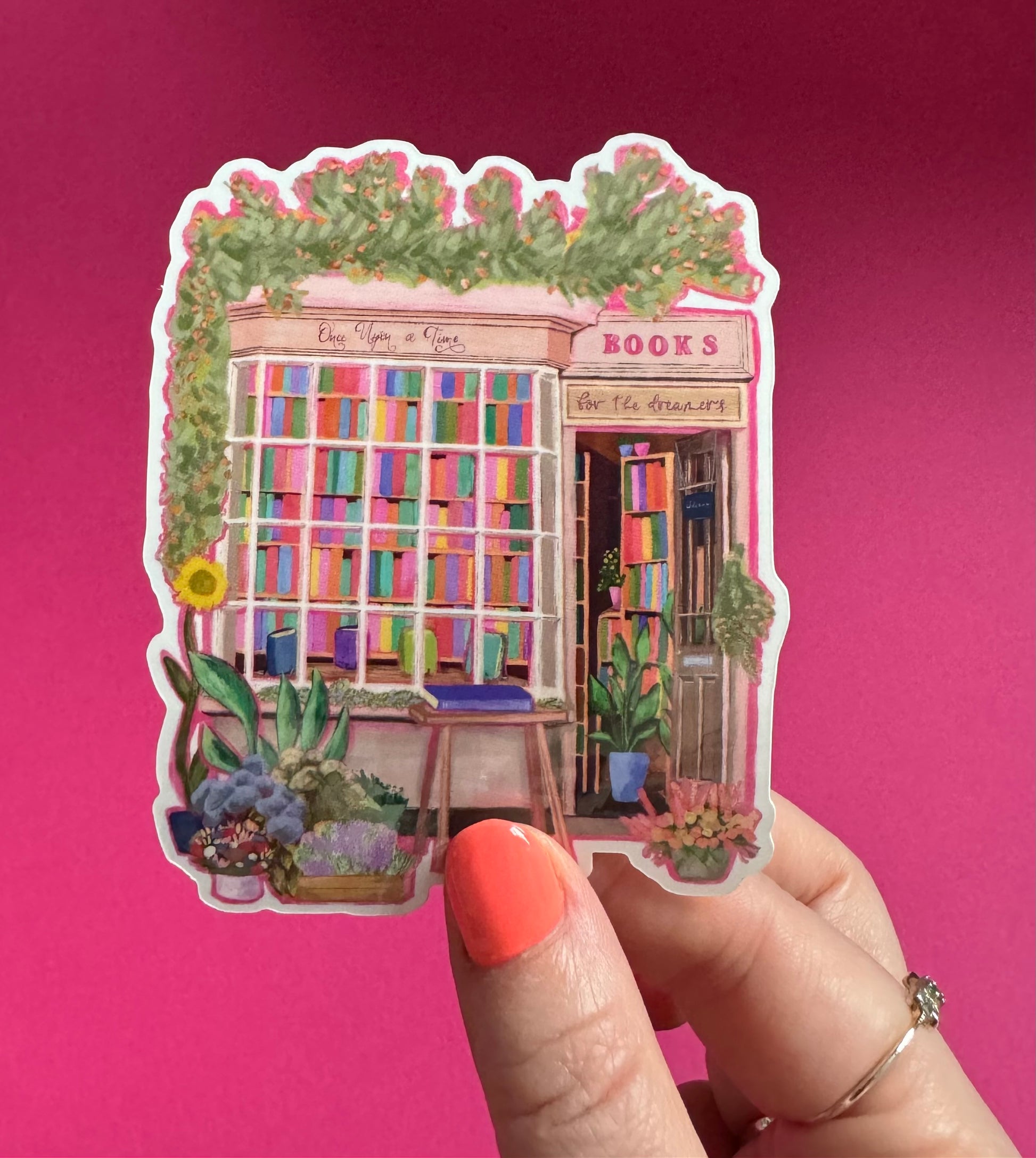 A sticker illustration of a cute bookshop, the window shows the bookshelves inside full of bright coloured book spines. There are books placed stood up at the front. Outside the building is a soft colour with lots of greenery in soft pale greens and orange and lilac flowers. In front of the building there are plant pots and flowers. Art sticker designed by Rebecca Gibbs at Rebecca Elizabeth Draws.