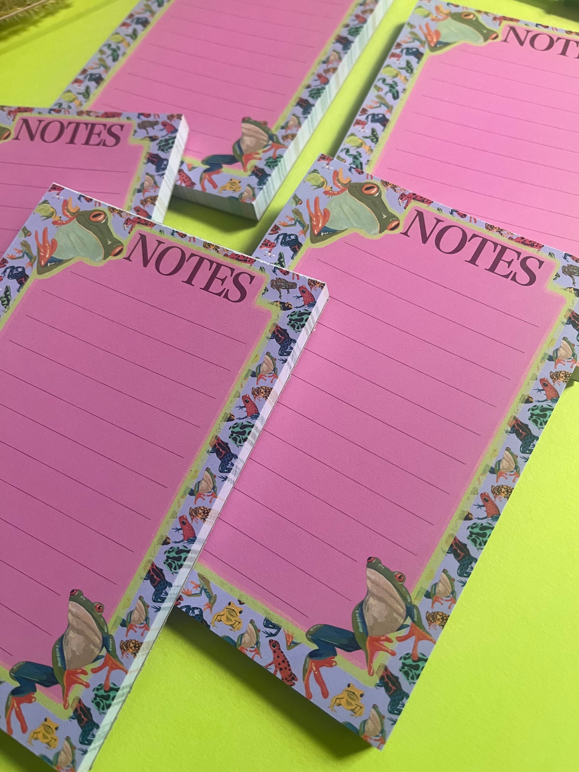 frog pattern notepad with purple background and a pink notes section. A couple of prominent frog’s peer around the notes. There is an accent colour of green, designed by Rebecca Elizabeth Draws.