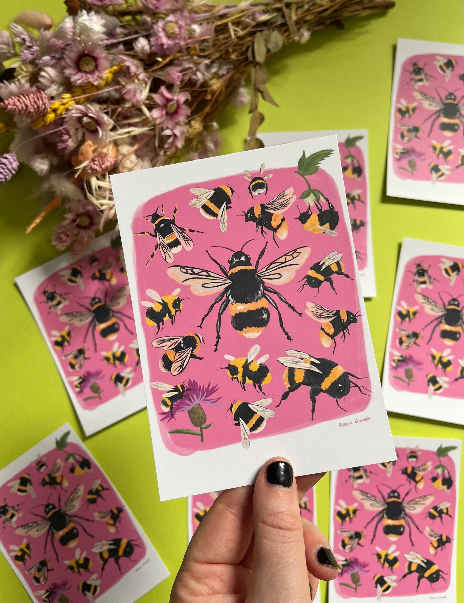 Hand painted bumble bee illustrations compiled together on a pink background, small bees big bees, bees with flowers. A big collection of bees illustrated by Rebecca Elizabeth Draws on a postcard. 