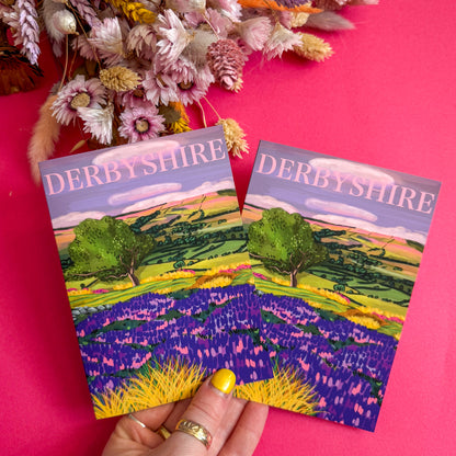 Two 'Derbyshire' postcards held against a pink background with flowers.