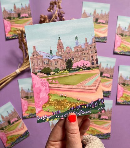 An illustration of the view of the Peace Gardens, Sheffield city centre in springtime. A soft brown building of Sheffield’s town hall with trees in front and pink blossom trees in soft pinks. The foreground features the peace garden with patches of grass and then flowers in yellows and purples underneath another pink blossom tree in the front and a baby blue sky. There is a small signature in white the corner.  Designed by Rebecca Gibbs on a postcard at Rebecca Elizabeth Draws.