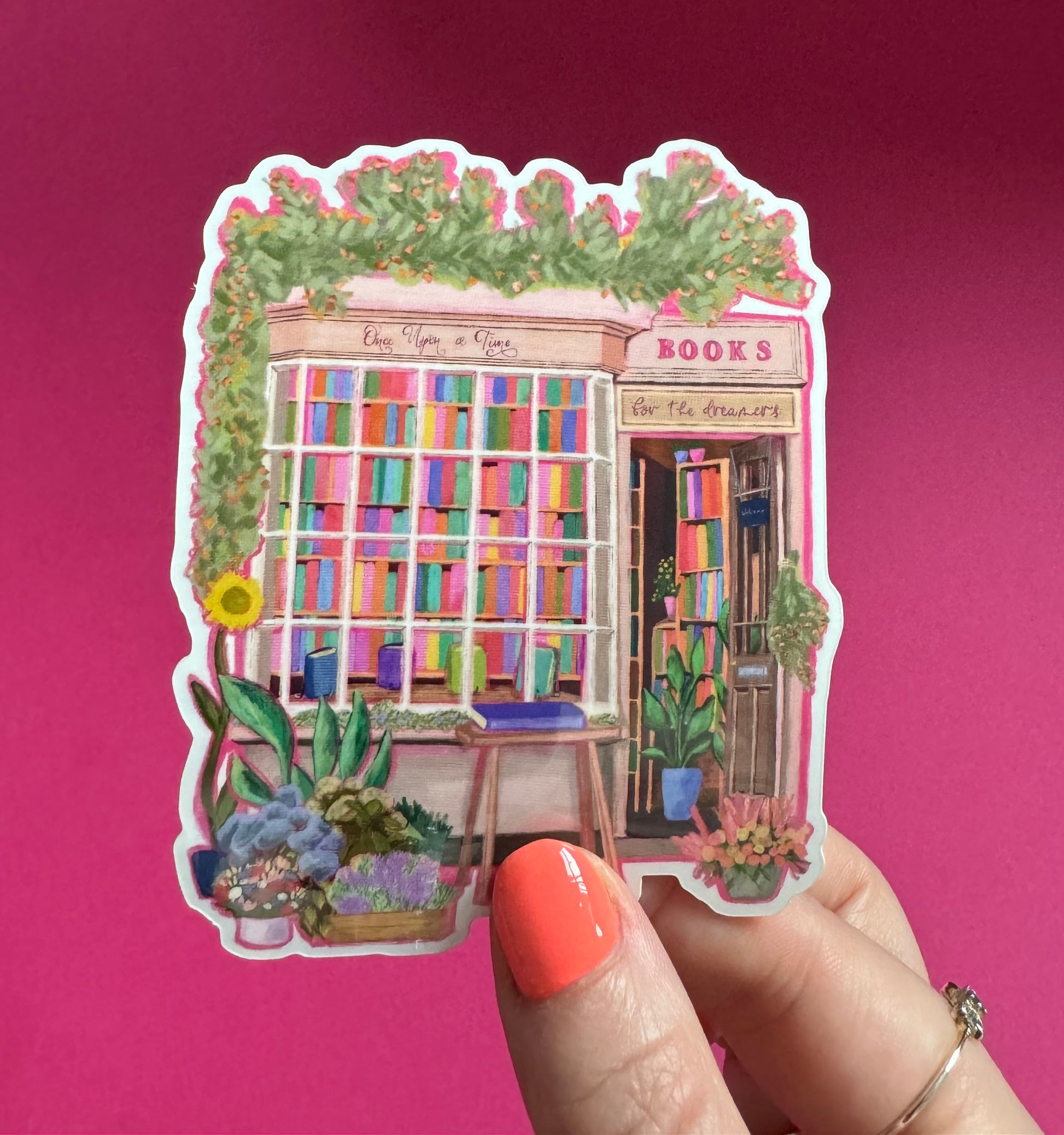 A sticker illustration of a cute bookshop, the window shows the bookshelves inside full of bright coloured book spines. There are books placed stood up at the front. Outside the building is a soft colour with lots of greenery in soft pale greens and orange and lilac flowers. In front of the building there are plant pots and flowers. Art sticker designed by Rebecca Gibbs at Rebecca Elizabeth Draws.