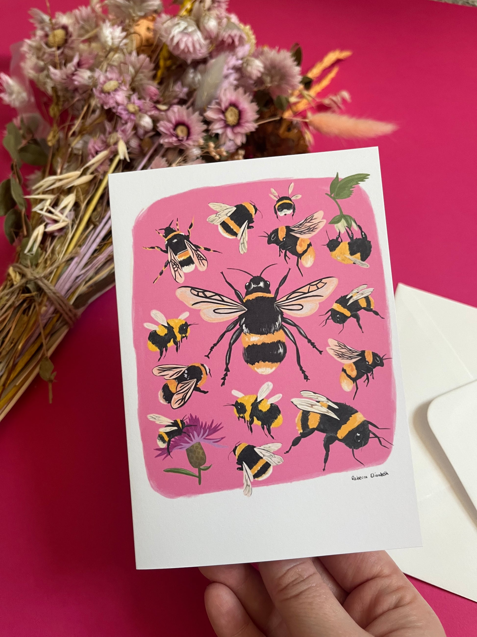 Hand painted bumble bee illustrations compiled together on a pink background, small bees big bees, bees with flowers. The back of the card is green with the Rebecca Elizabeth Draws logo