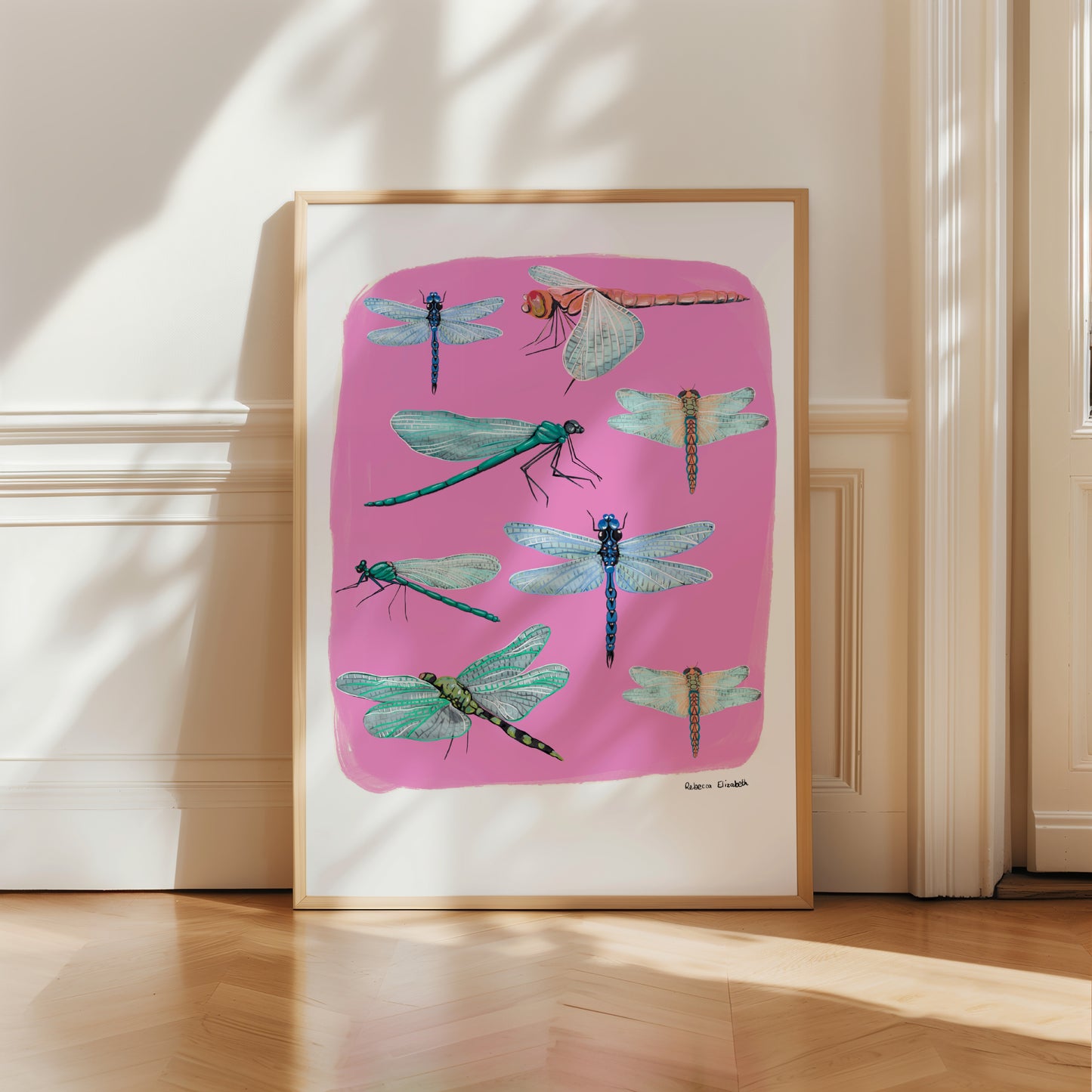 Hand painted dragonflies in gouache and edited digitally onto soft coloured pink backgrounds. Dragonflies in a flat lay composition with lots of intricate details featured. There is a small signature in black at the right.  Designed by Rebecca Gibbs at Rebecca Elizabeth Draws. 