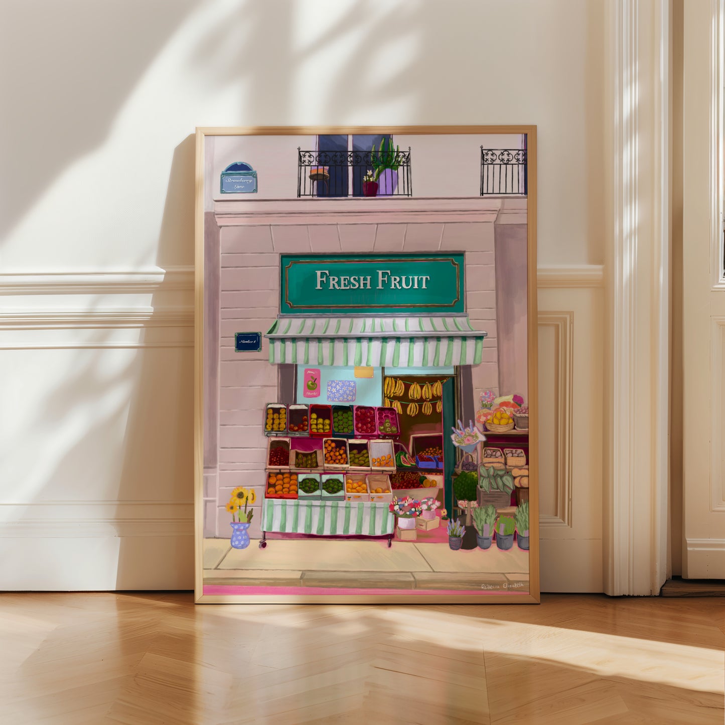 Illustration of a fabulous fruit shop, baskets of fruit line outside the shop, a canopy in mint green & white hangs over & inside you can see boxes of fruit & bananas hanging. The wall has a sign strawberry lane & there is a balcony upstairs. 