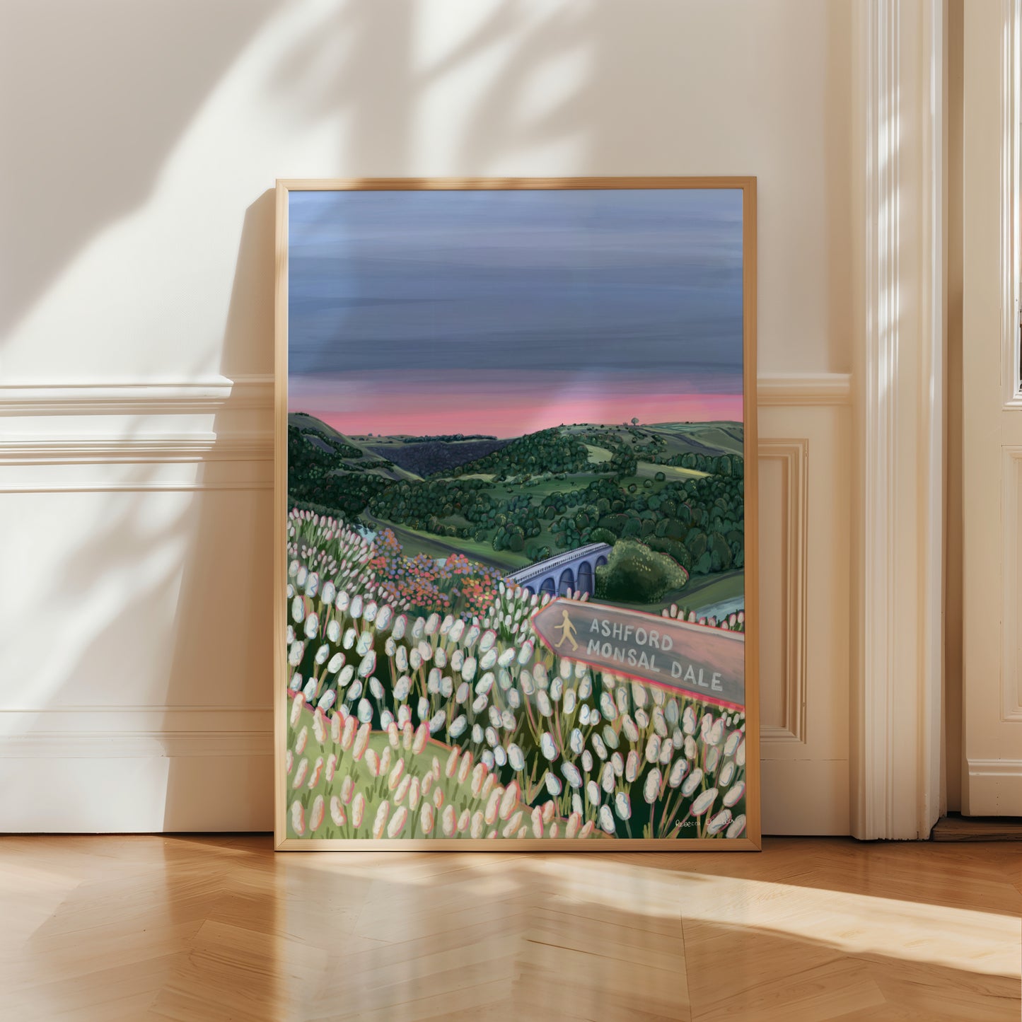 An illustration of Monsal Head in Derbyshire, Peak District. Rolling green hills filled with trees, an old viaduct over the river Wye and white flowers in the foreground. The sky is a setting sun with pink on the horizon fading into dark blue grey. 