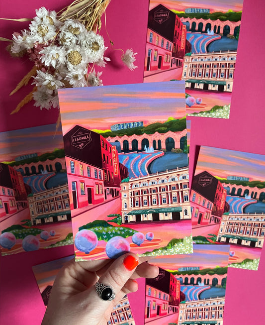 Postcard of an illustration of the Sheffield city with The Lyceum theatre, The Leadmill venue, the train station, park hill flats & graffiti. Designed by Rebecca Elizabeth Draws. Vibrant pinks, purples and oranges are featured. 