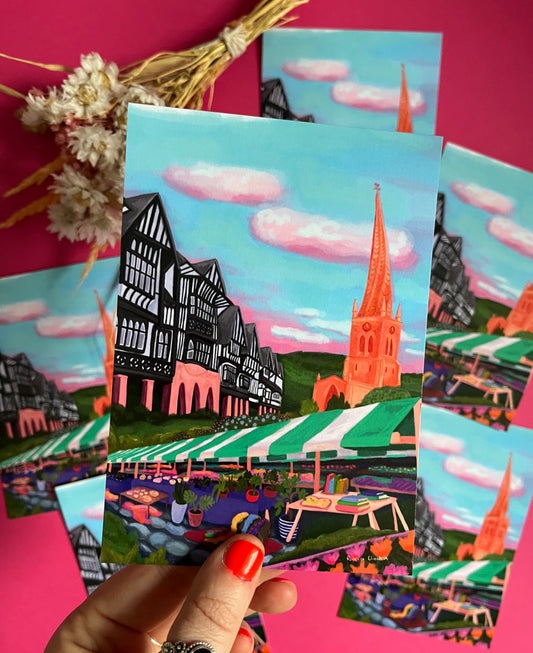 Postcard of an illustration of Chesterfield, Derbyshire town. Featuring the crooked spire, the Tudor buildings, the market, and the peak district hills. Set against a blue sky with fluffy white clouds. Designed by Rebecca Elizabeth Draws. 