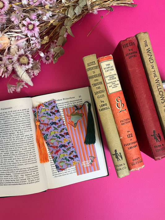 An illustration of frogs on a bookmark. A colourful frog pattern on a purple background on the front and a purple and orange stripe pattern on the back featuring some sneaky peak frogs alongside the Rebecca Elizabeth draws logo. Designed by Rebecca Gibbs at Rebecca Elizabeth Draws.