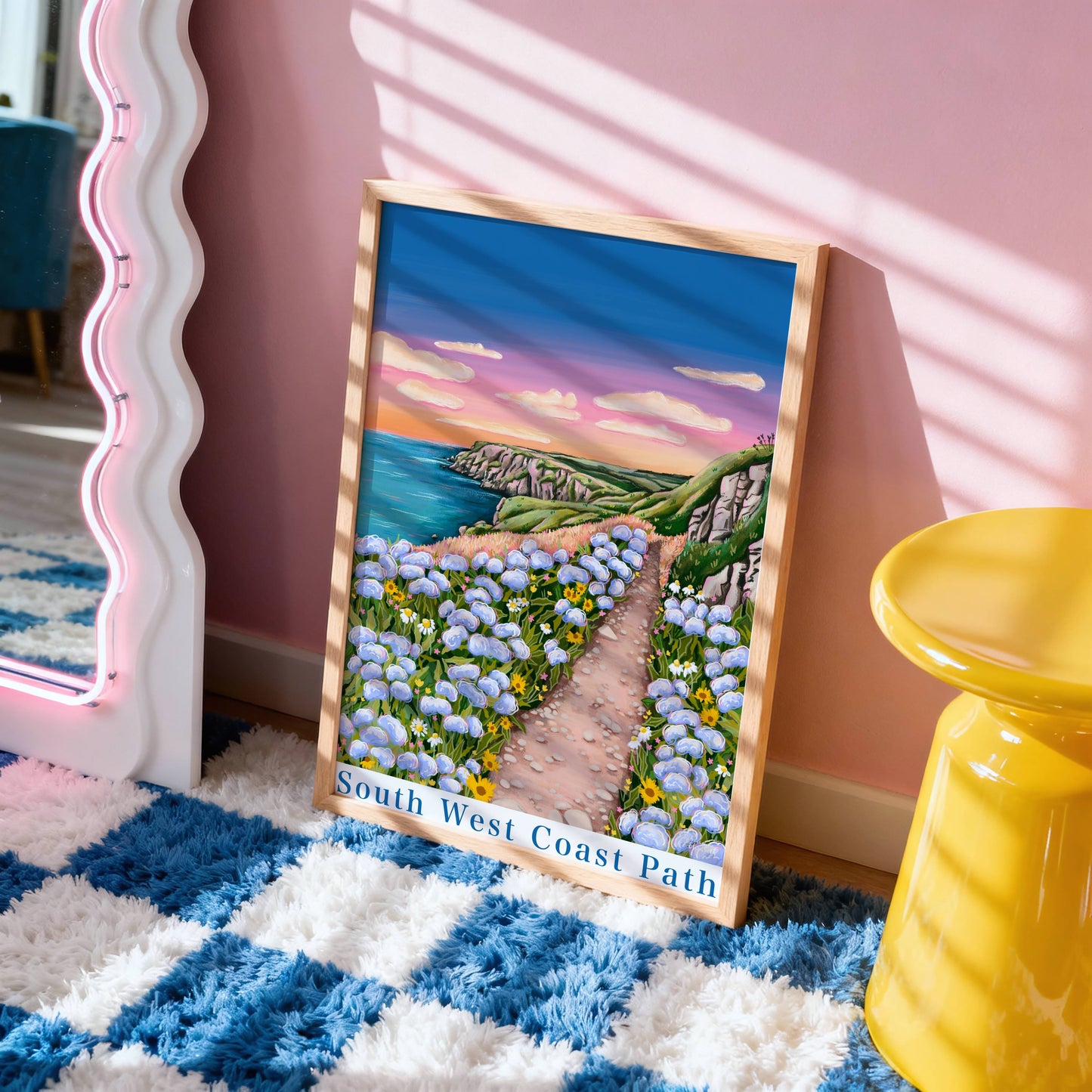 Framed artwork of a scenic path with flowers on a blue and white checkered rug.