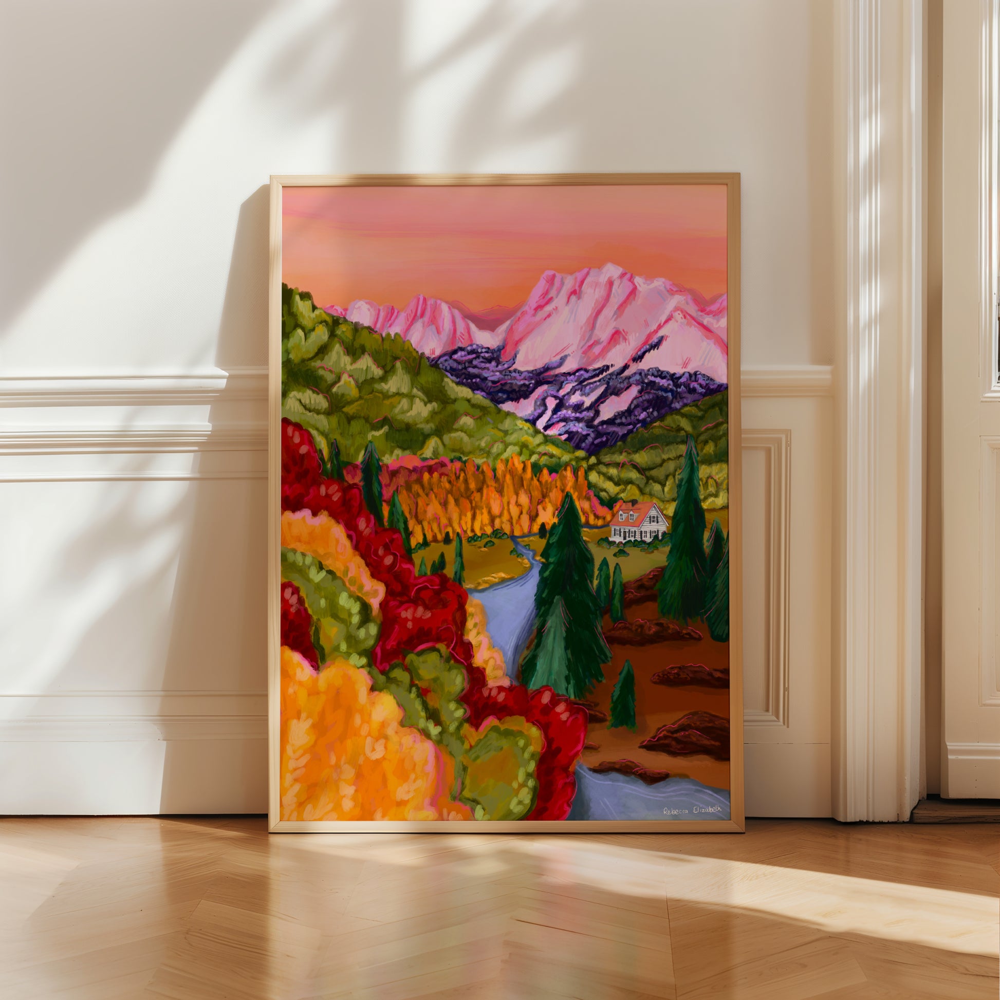 Pink, orange, red, brown and yellow mountain landscape illustration with autumnal trees and leaves. A cute cosy cabin sits nestled at the bottom of the mountains amongst the forest and a river runs alongside. Inspired by Colorado USA.