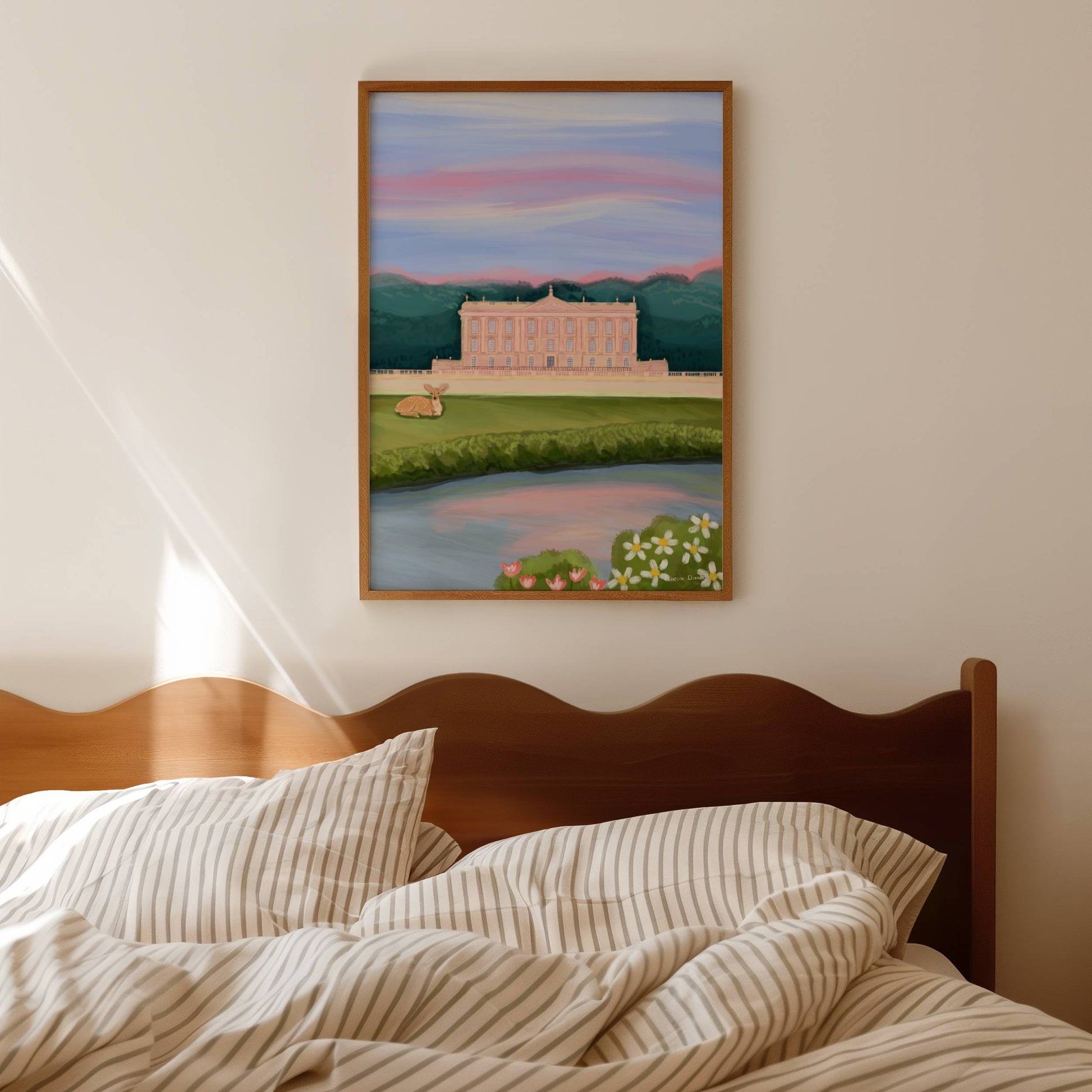 An illustration of Chatsworth house, a stately home found in the Derbyshire Dales. The house is a soft pink surrounded by green trees and fields, a river runs along the front and a deer rests in the foreground. The sky is a soft blue and pink hue, the colours of a beautiful sunset. A small signature in white the corner.  Designed by Rebecca Gibbs at Rebecca Elizabeth Draws.